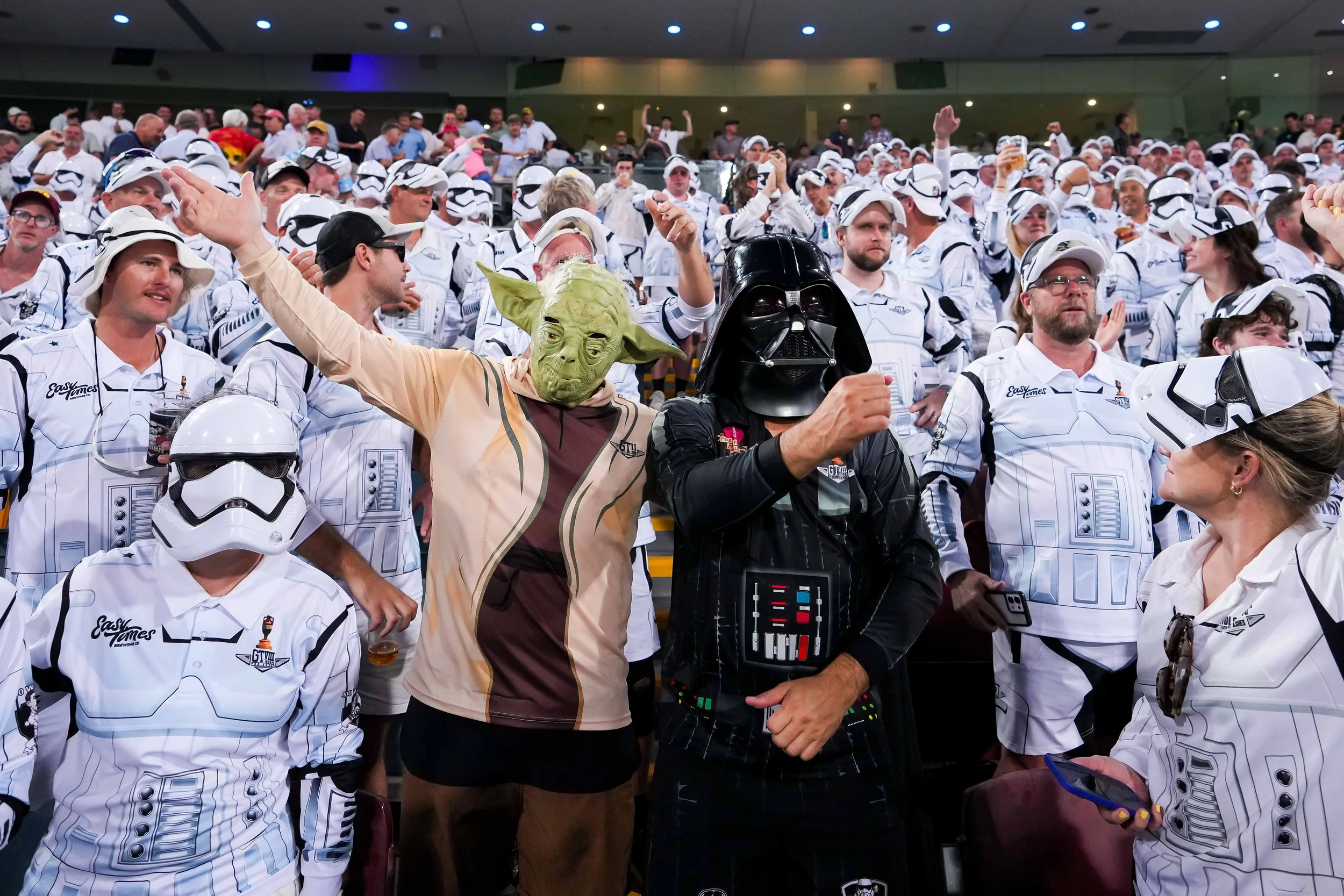 People dressed as Yoda and Darth Vader from Star Wars at a crowded event, with many individuals wearing Star Wars-themed costumes and hats.
