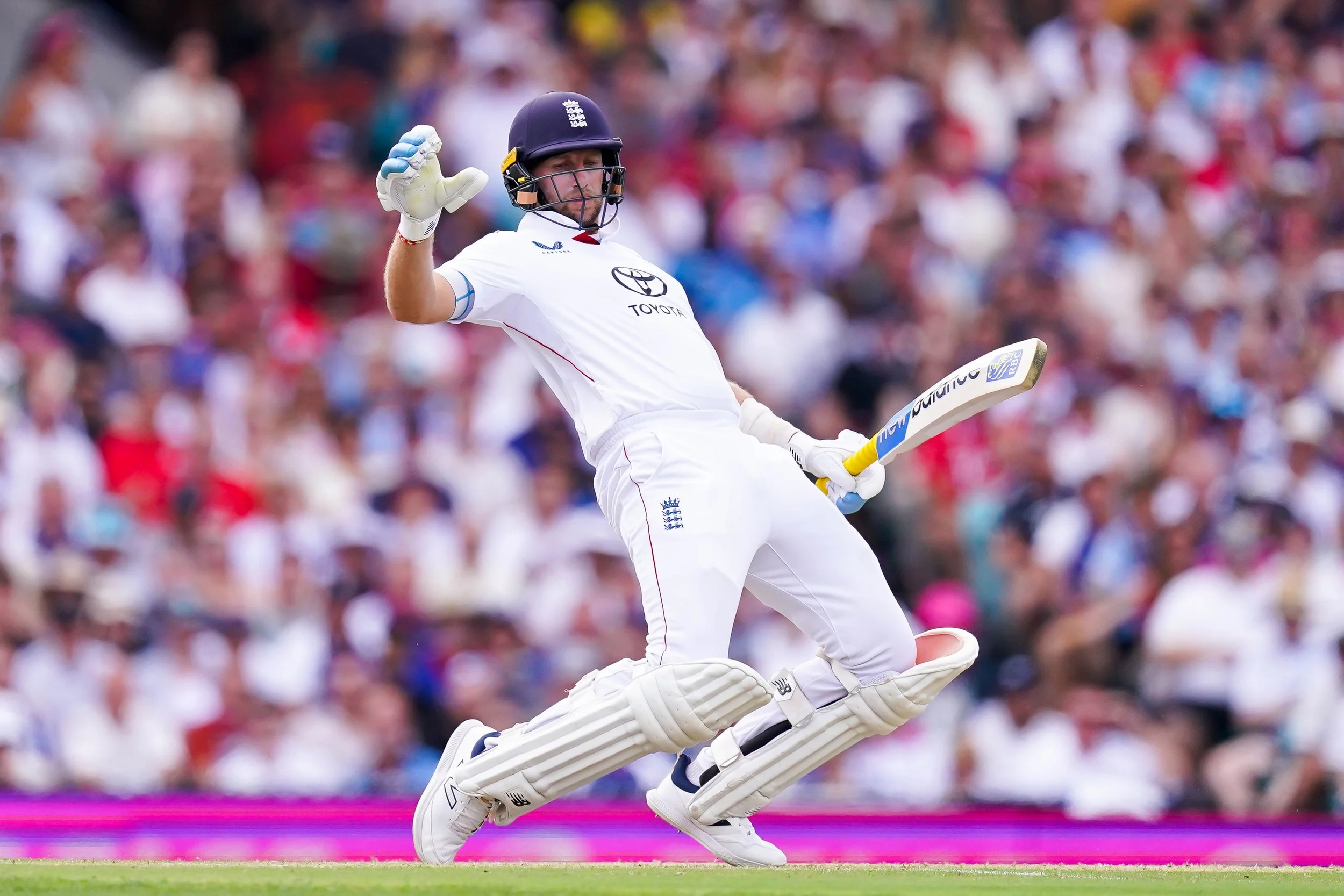 Cricket player in white uniform and helmet runs with bat while crossing the pitch, with a packed crowd in the background.