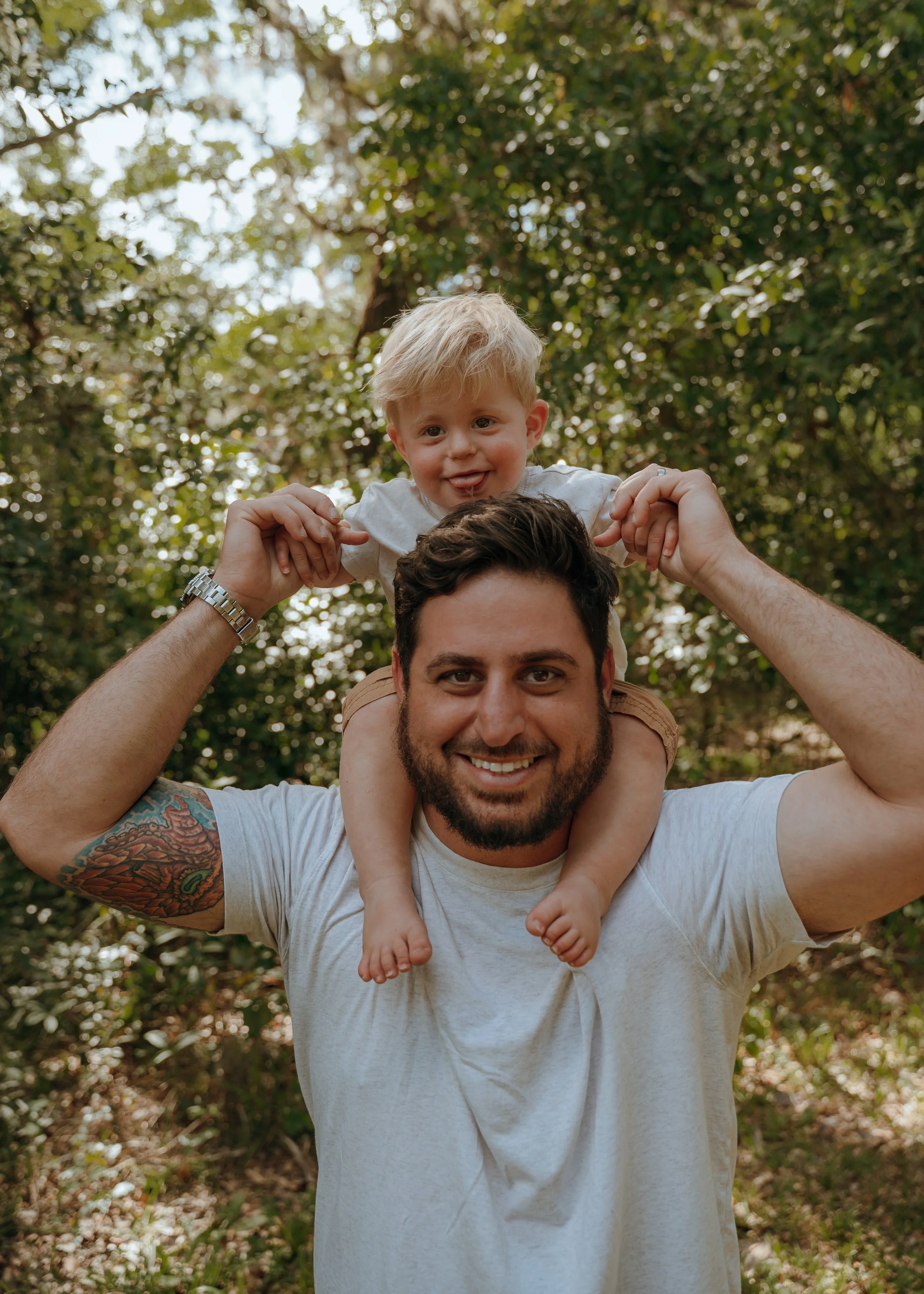 Father smiling with his young son riding on his shoulders during an outdoor family session in Palm Beach County.