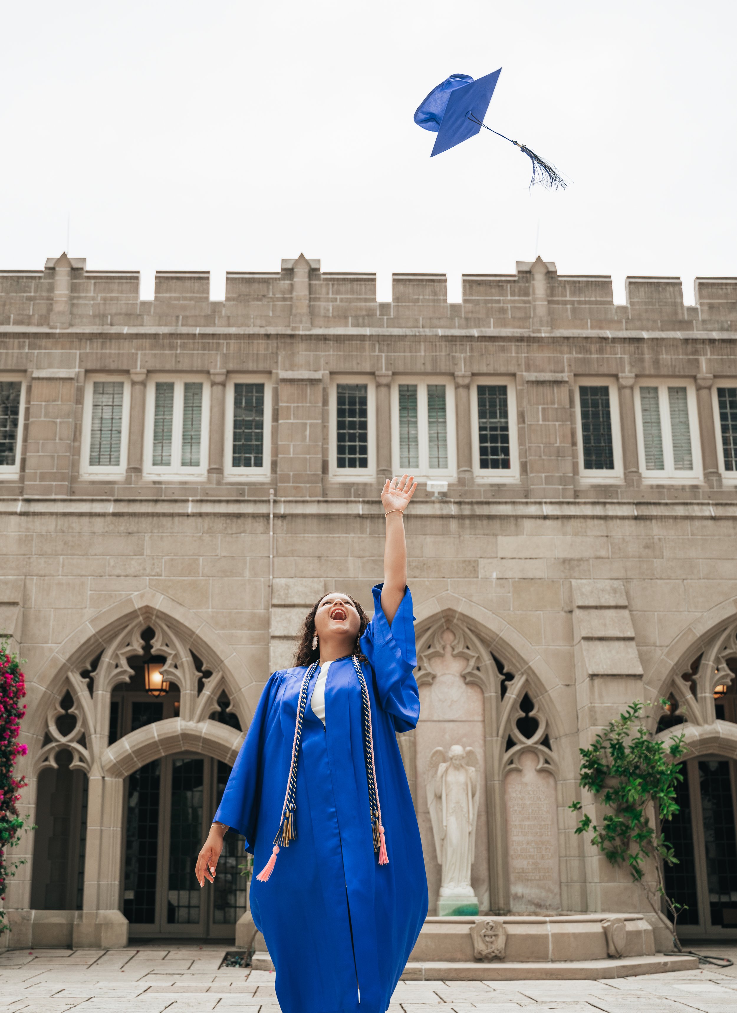 Graduate in a royal blue cap and gown tossing her graduation cap outside Bethesda-by-the-Sea in Palm Beach, Florida.