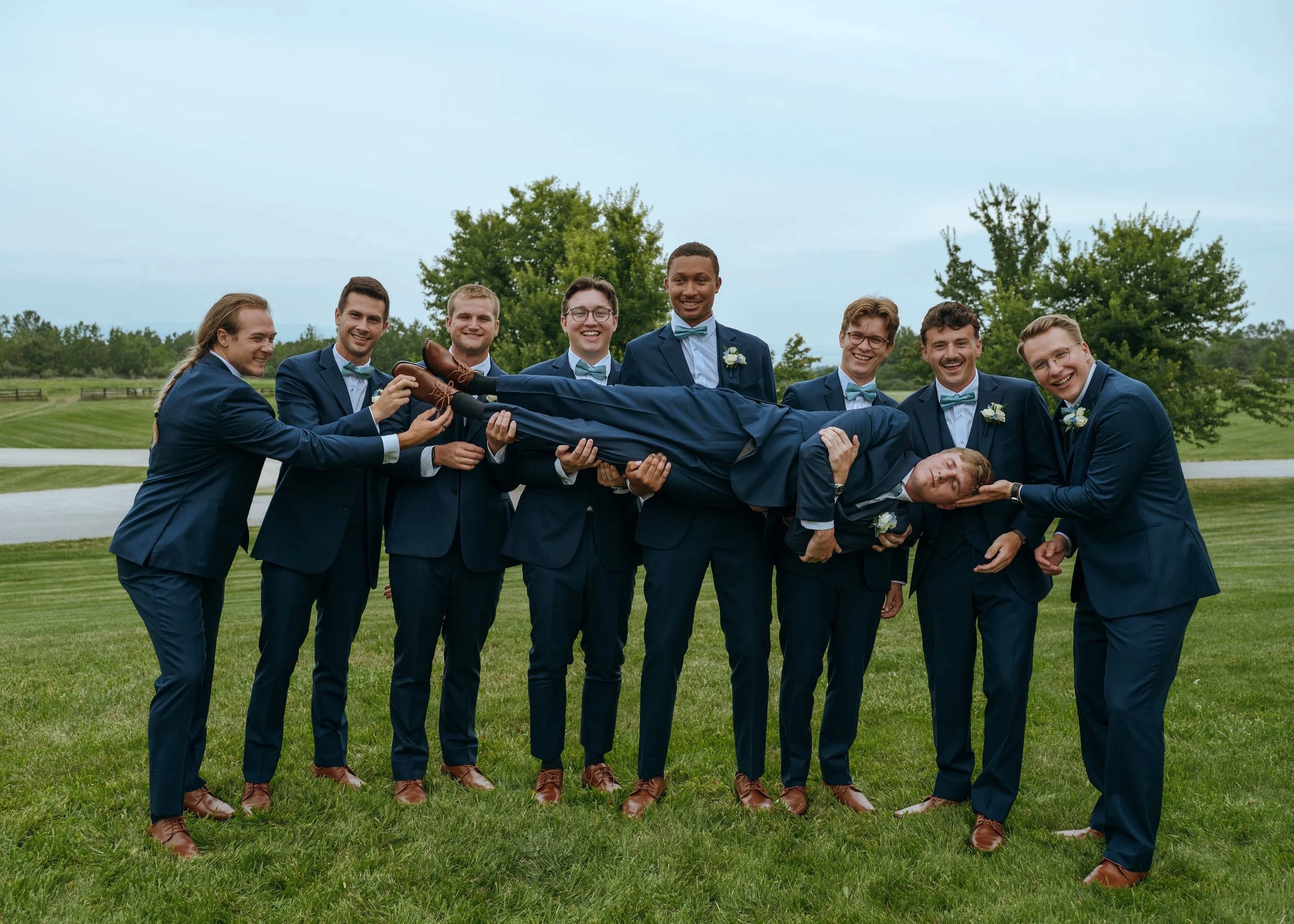 Matt’s groomsmen lift him during a playful wedding-party portrait outside Gypsy Distillery.