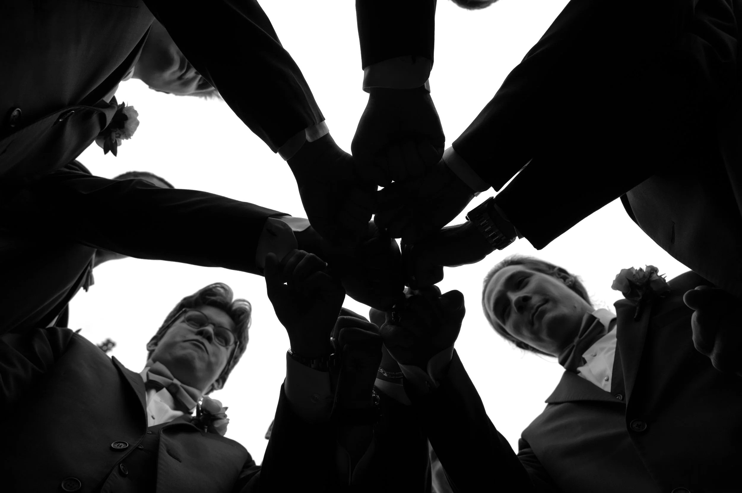 Black-and-white view looking up at Matt and his groomsmen gathered in a circle at Gypsy Distillery.