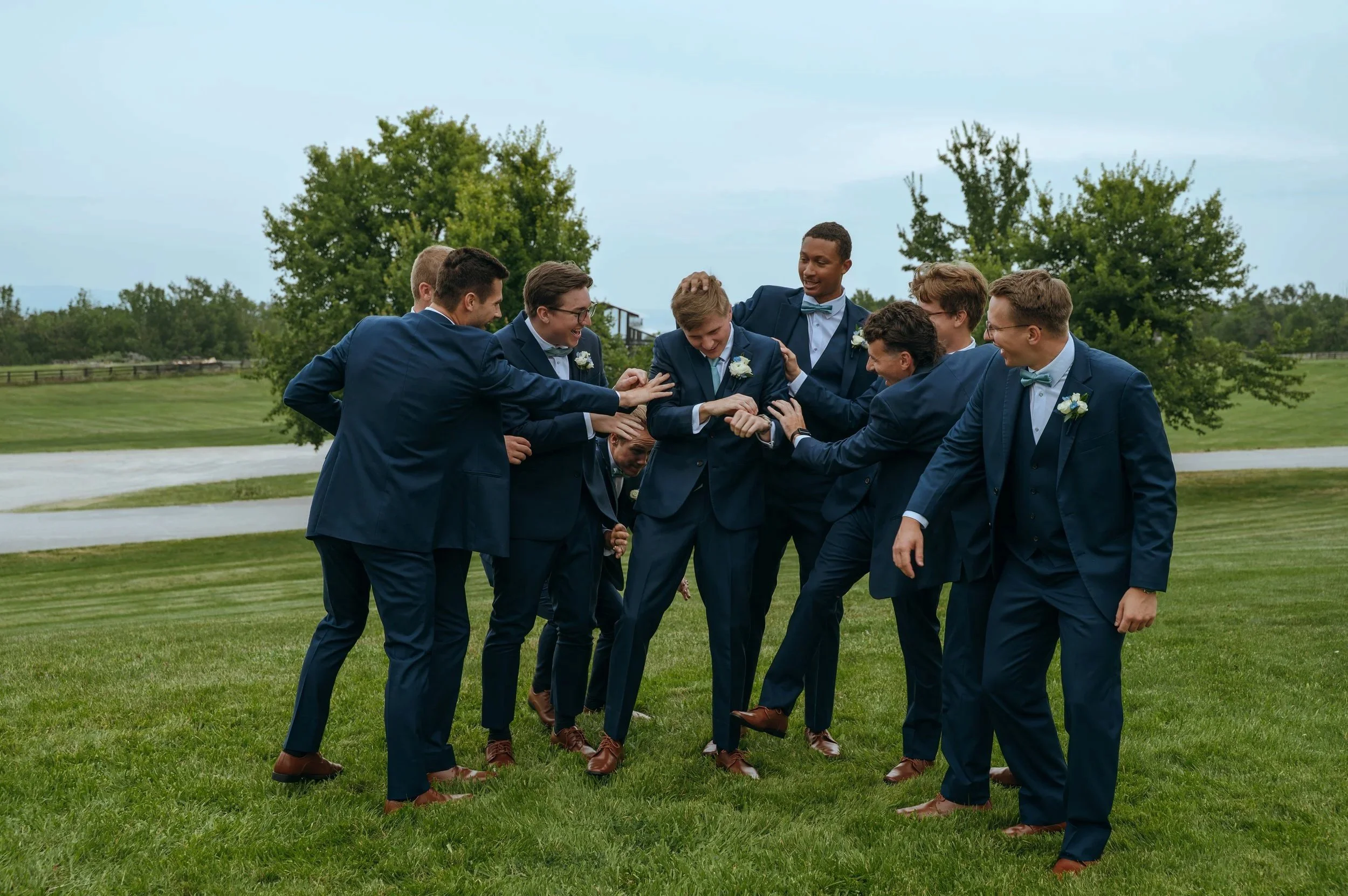 Matt laughs with his groomsmen during playful wedding-party portraits outside Gypsy Distillery in Petoskey, Michigan.
