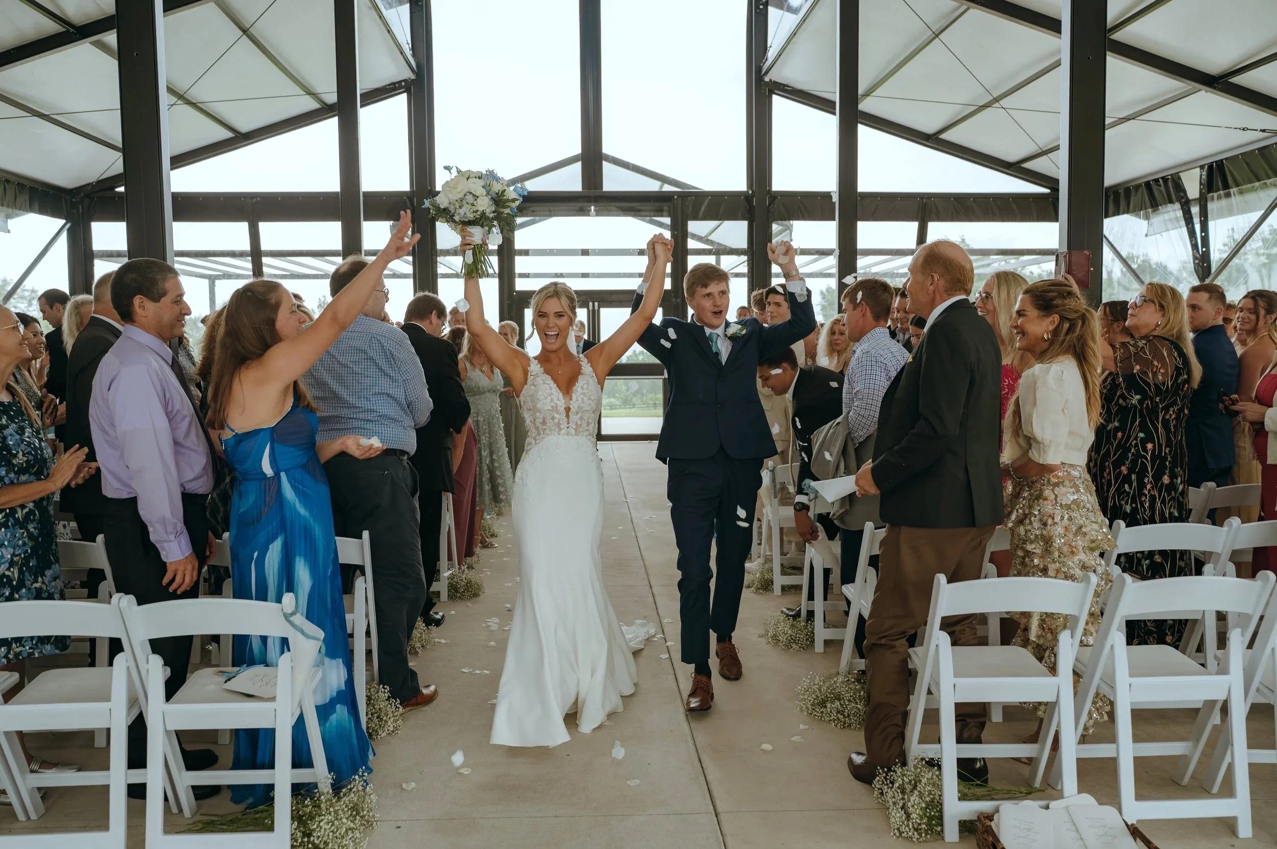 Guests raise their hands and celebrate as Sydney and Matt walk back up the aisle at Gypsy Distillery.