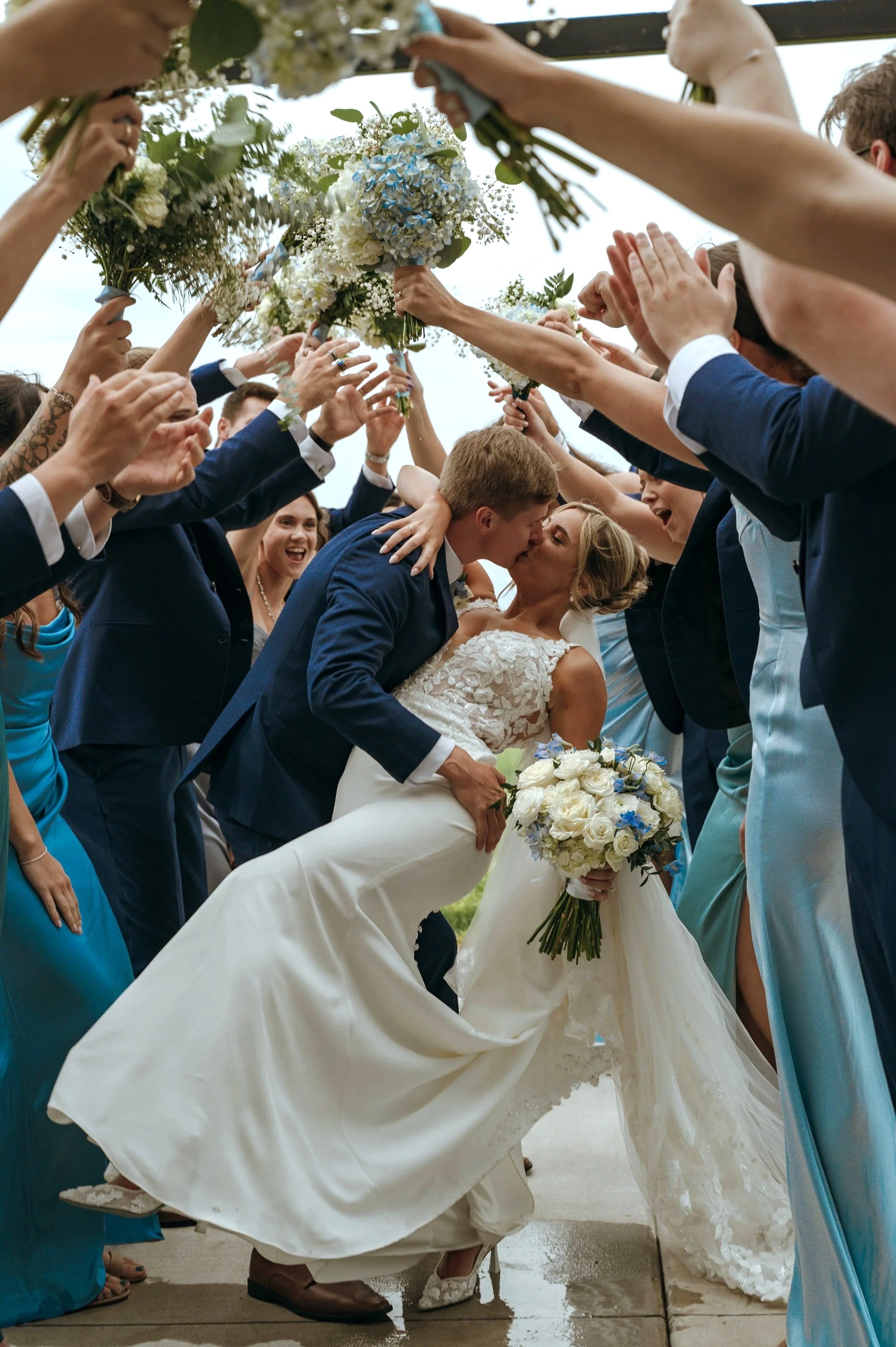 Sydney and Matt kiss beneath raised bouquets held by their wedding party at Gypsy Distillery.
