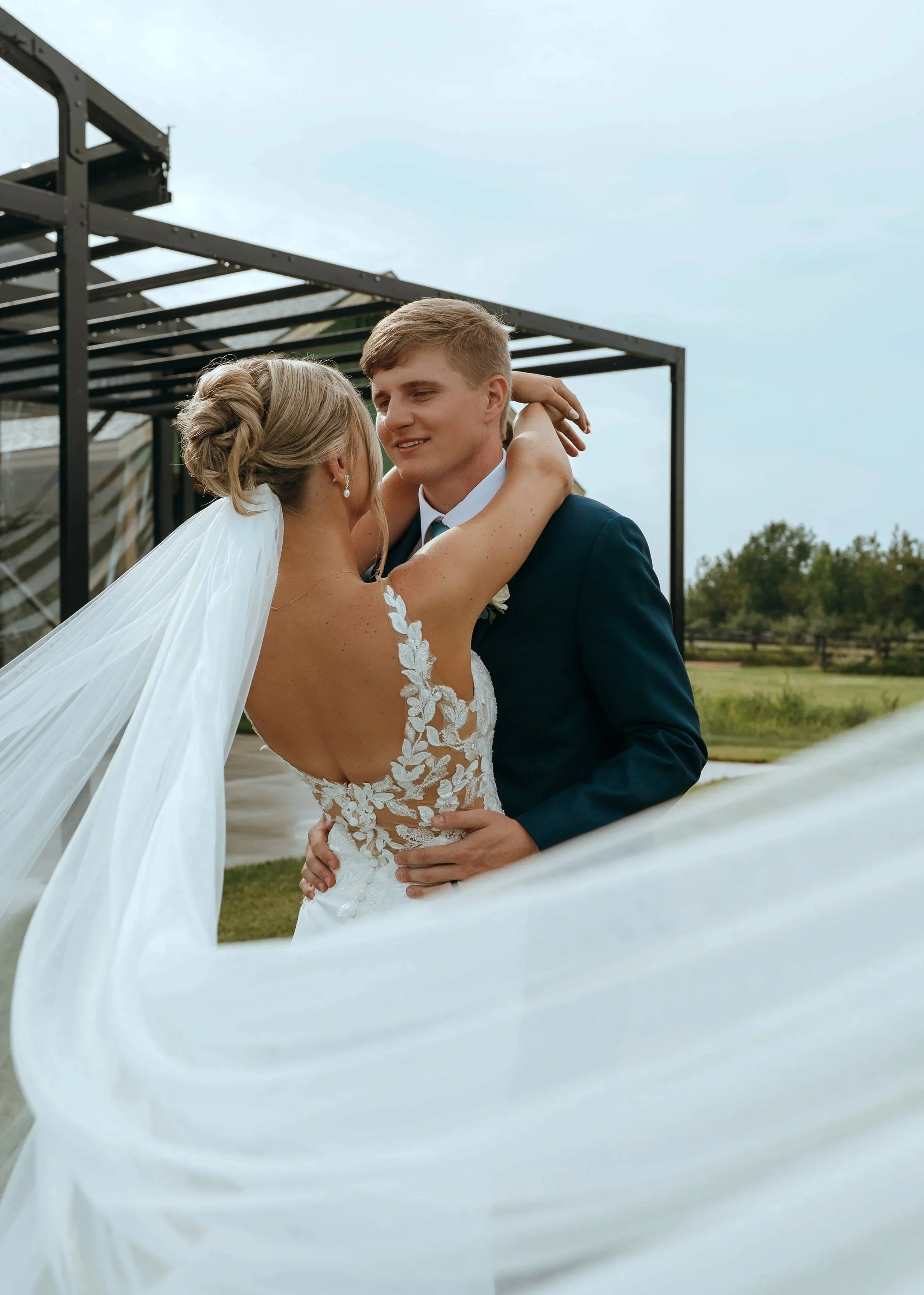 Sydney wraps her arms around Matt as her veil moves through the foreground at Gypsy Distillery.