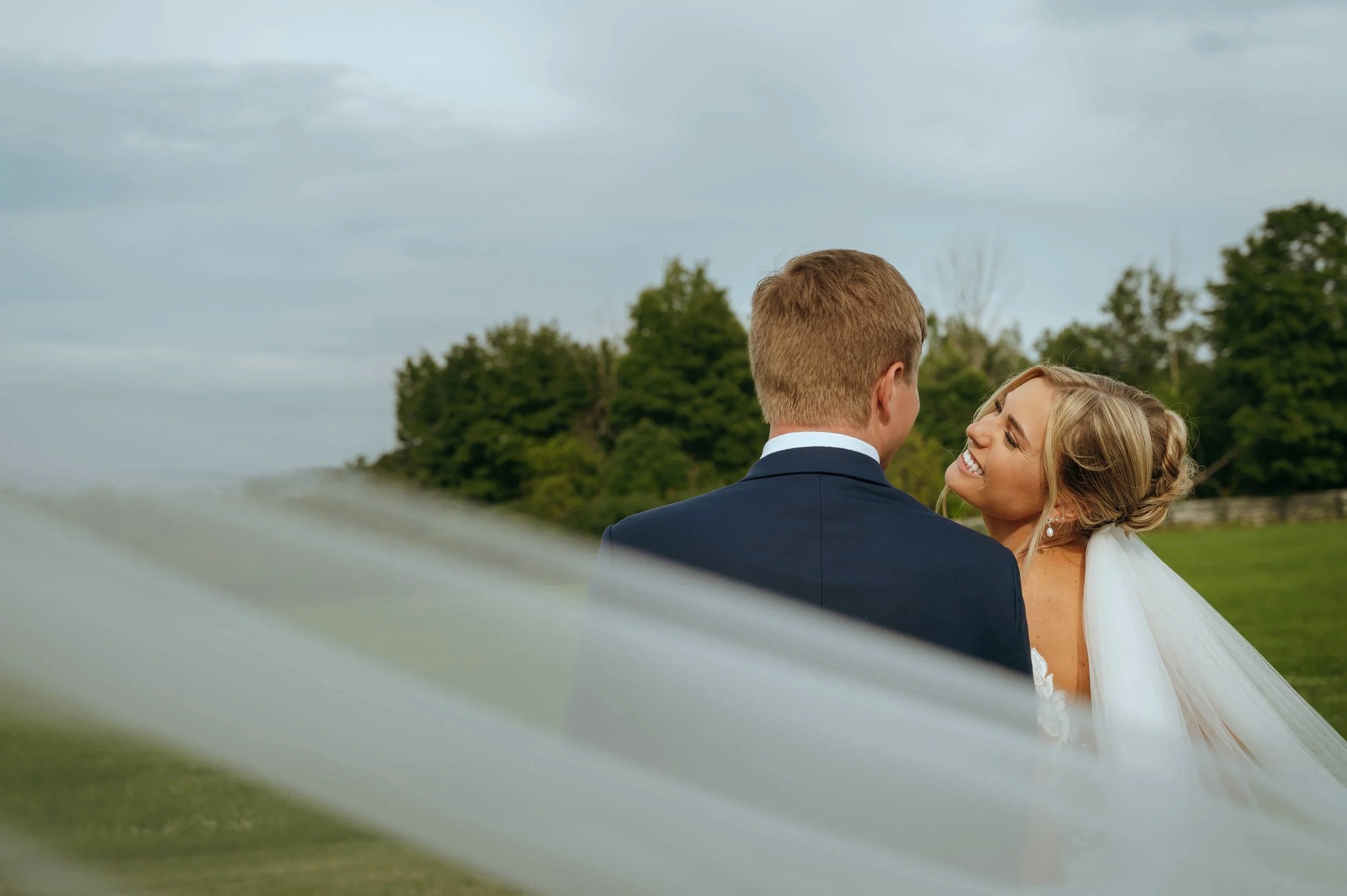 Sydney kisses Matt’s cheek during an intimate wedding portrait framed by her veil in Petoskey, Michigan.