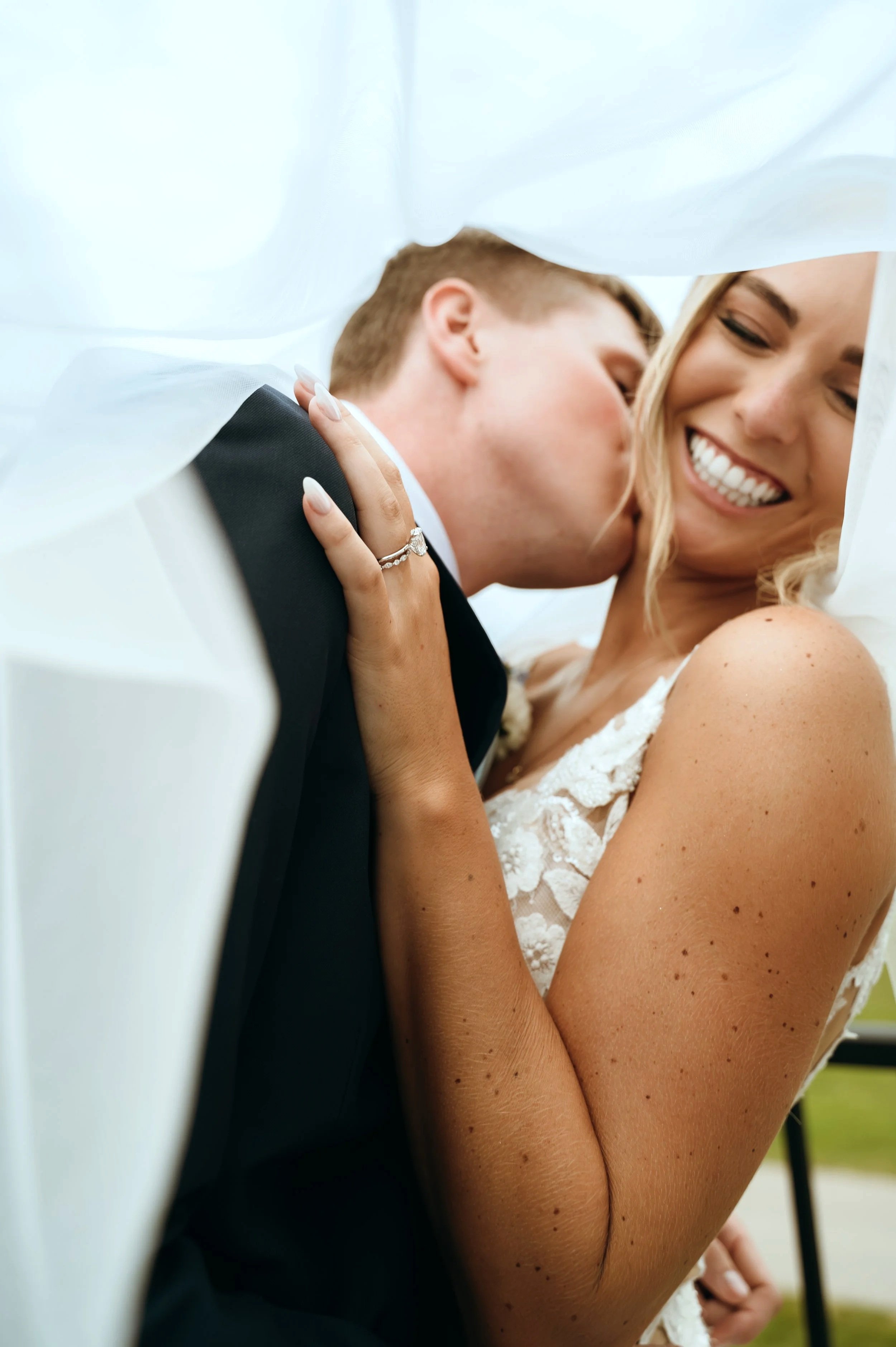 Matt kisses Sydney’s cheek as she laughs during their rooftop wedding portraits in Petoskey, Michigan.