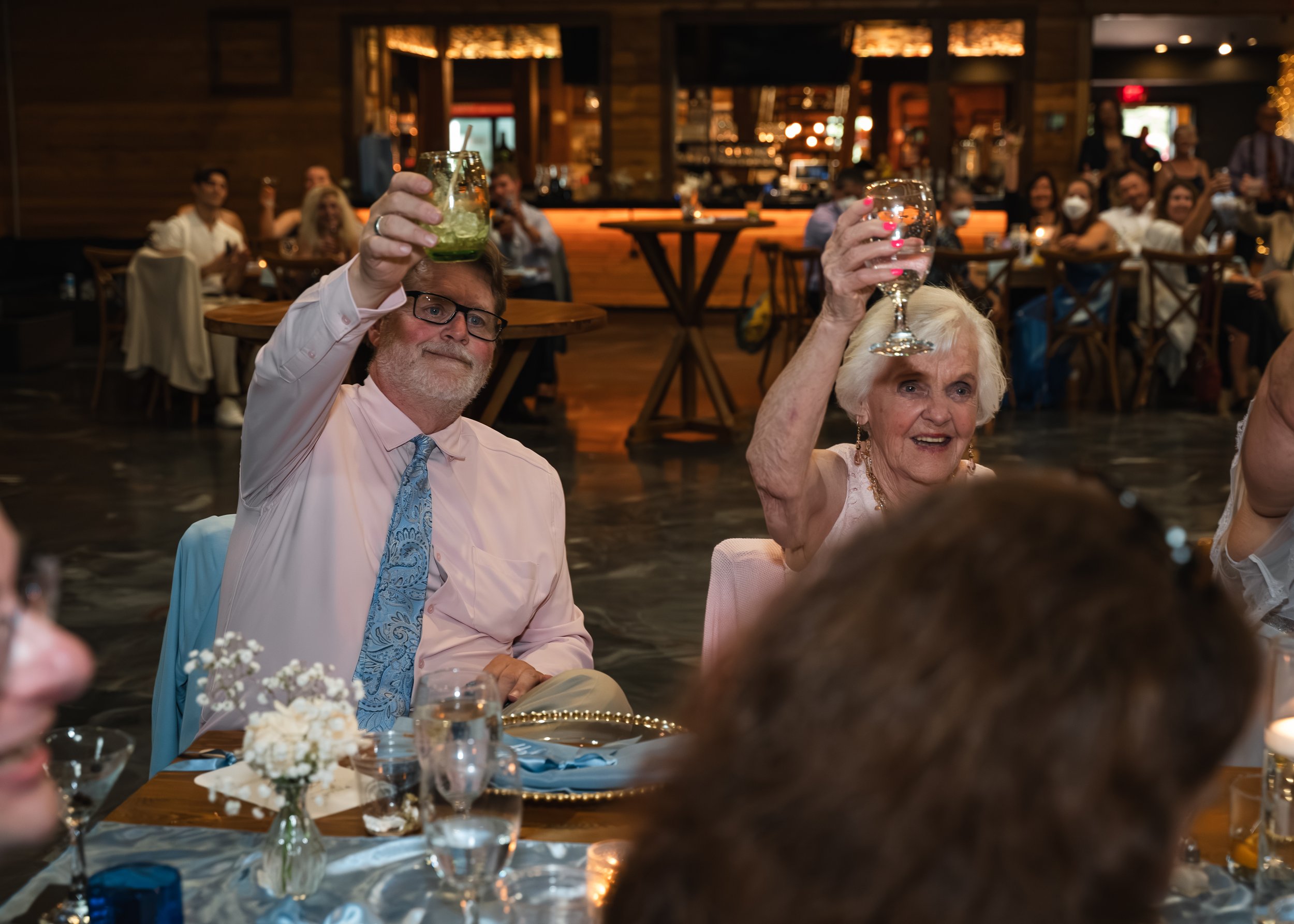 Wedding guests raise colorful vintage glasses during a reception toast at Gypsy Distillery.