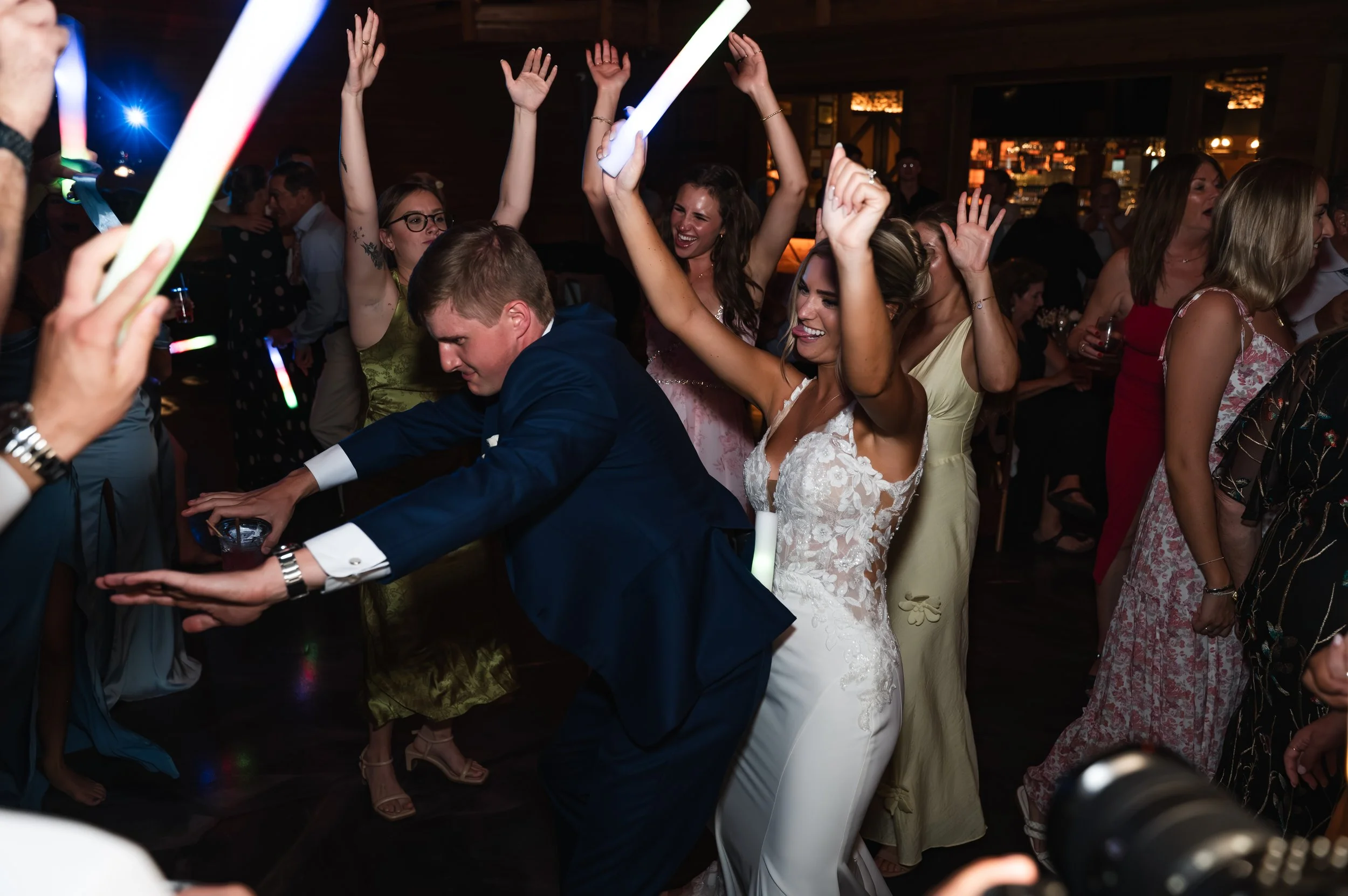 Sydney and Matt dance with raised hands and glow sticks during their Gypsy Distillery wedding reception.