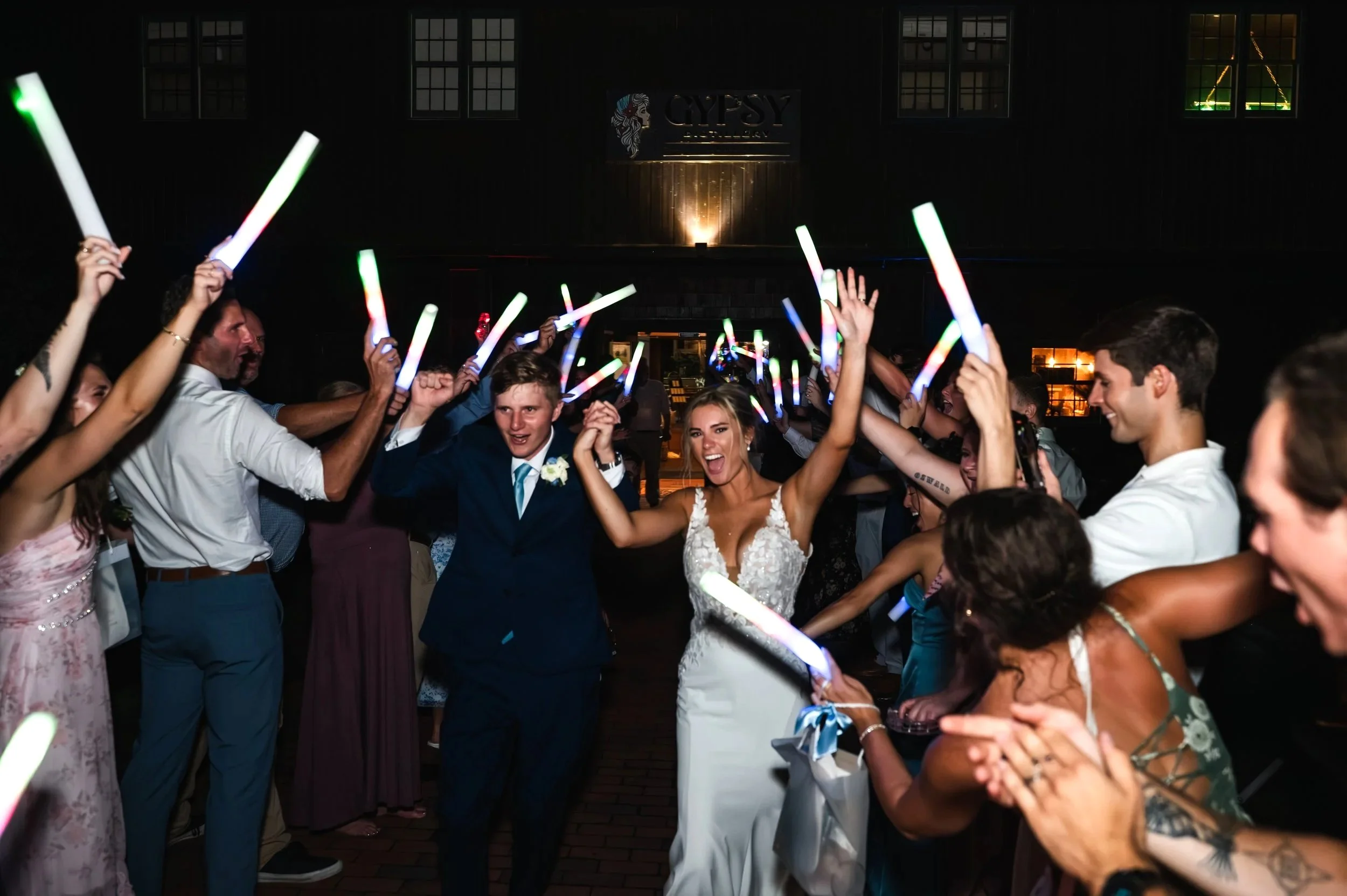 Sydney and Matt walk between guests holding glow sticks outside Gypsy Distillery in Petoskey, Michigan.