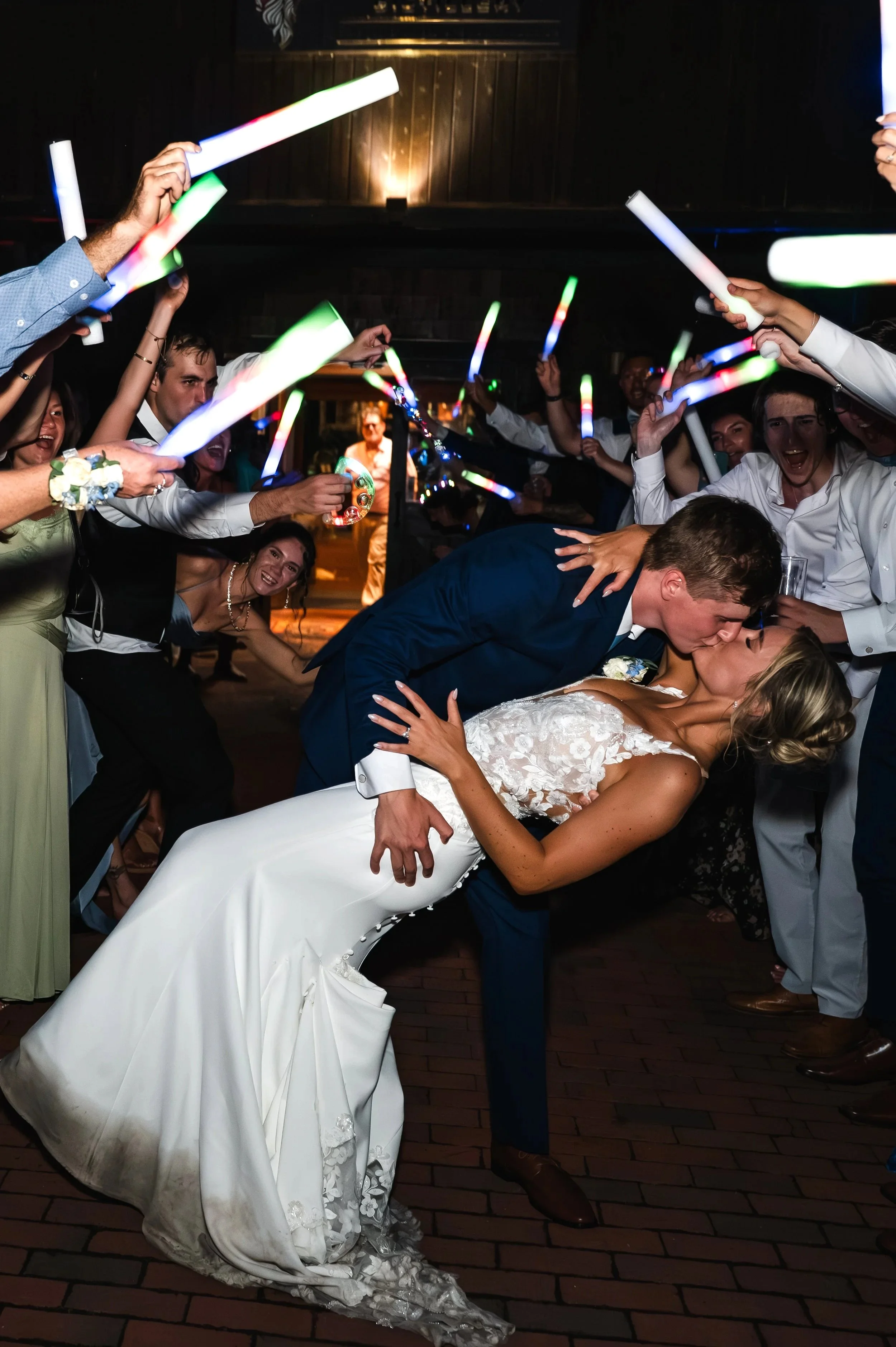 Sydney and Matt share a dip kiss beneath raised glow sticks during their wedding exit.