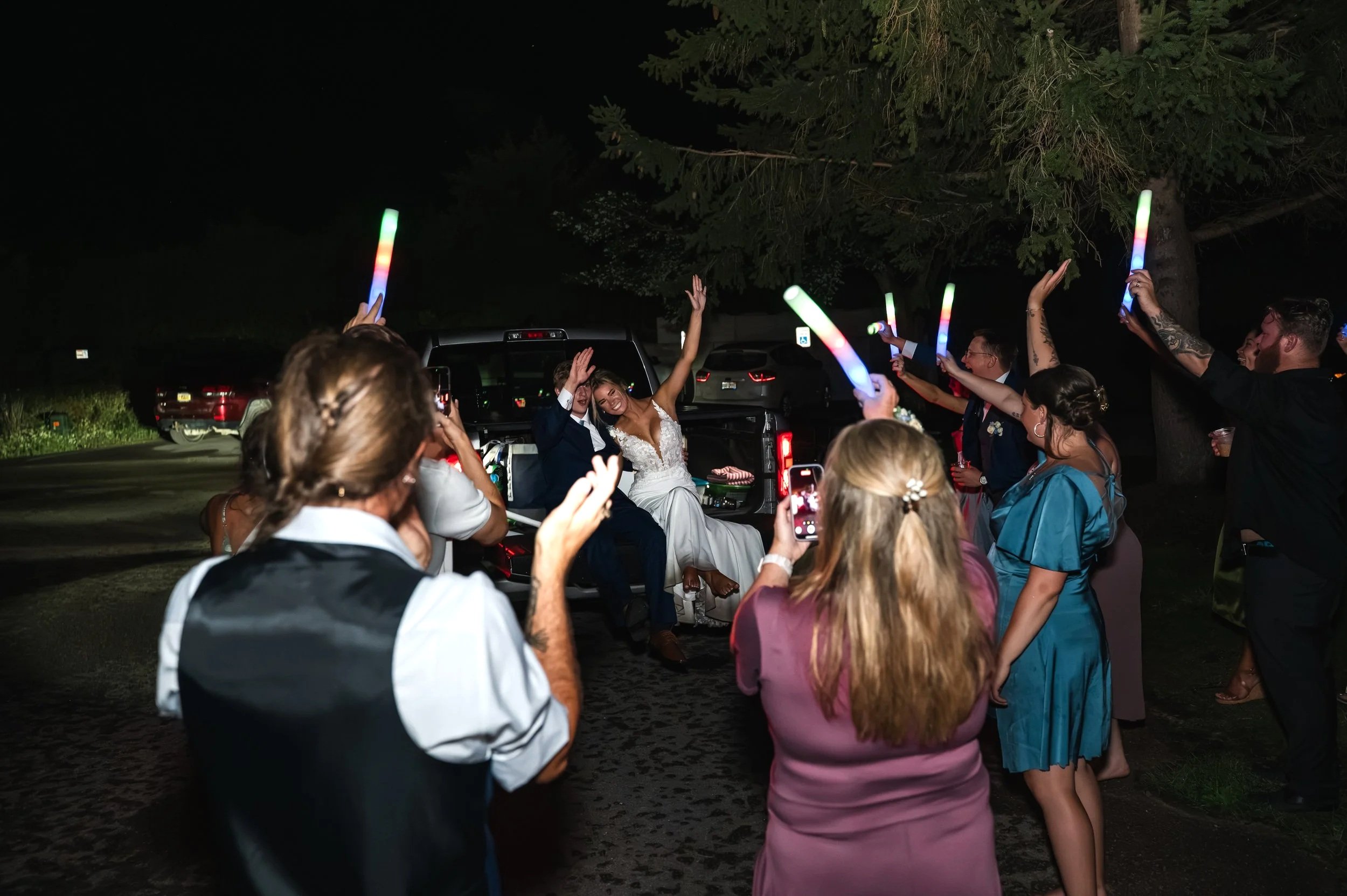 Guests wave glow sticks as Sydney and Matt prepare to leave their Gypsy Distillery wedding in a pickup truck.