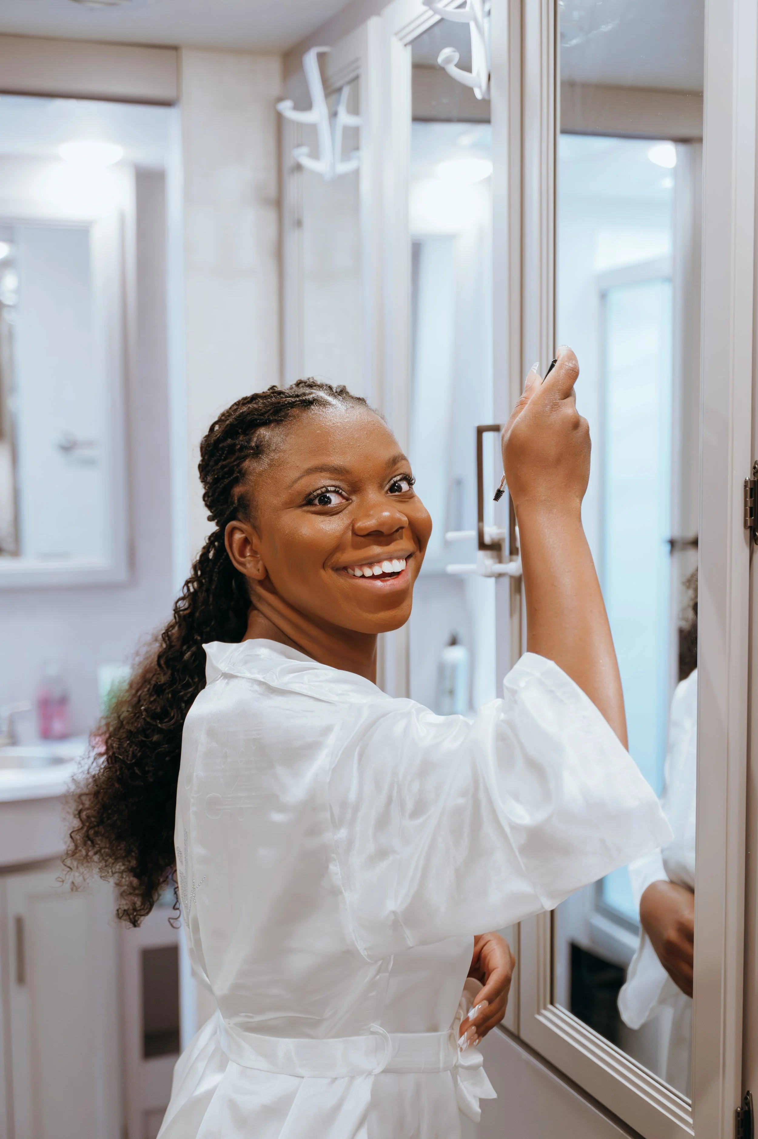 Anndi smiles toward the camera while getting ready beside a mirror on her wedding morning.