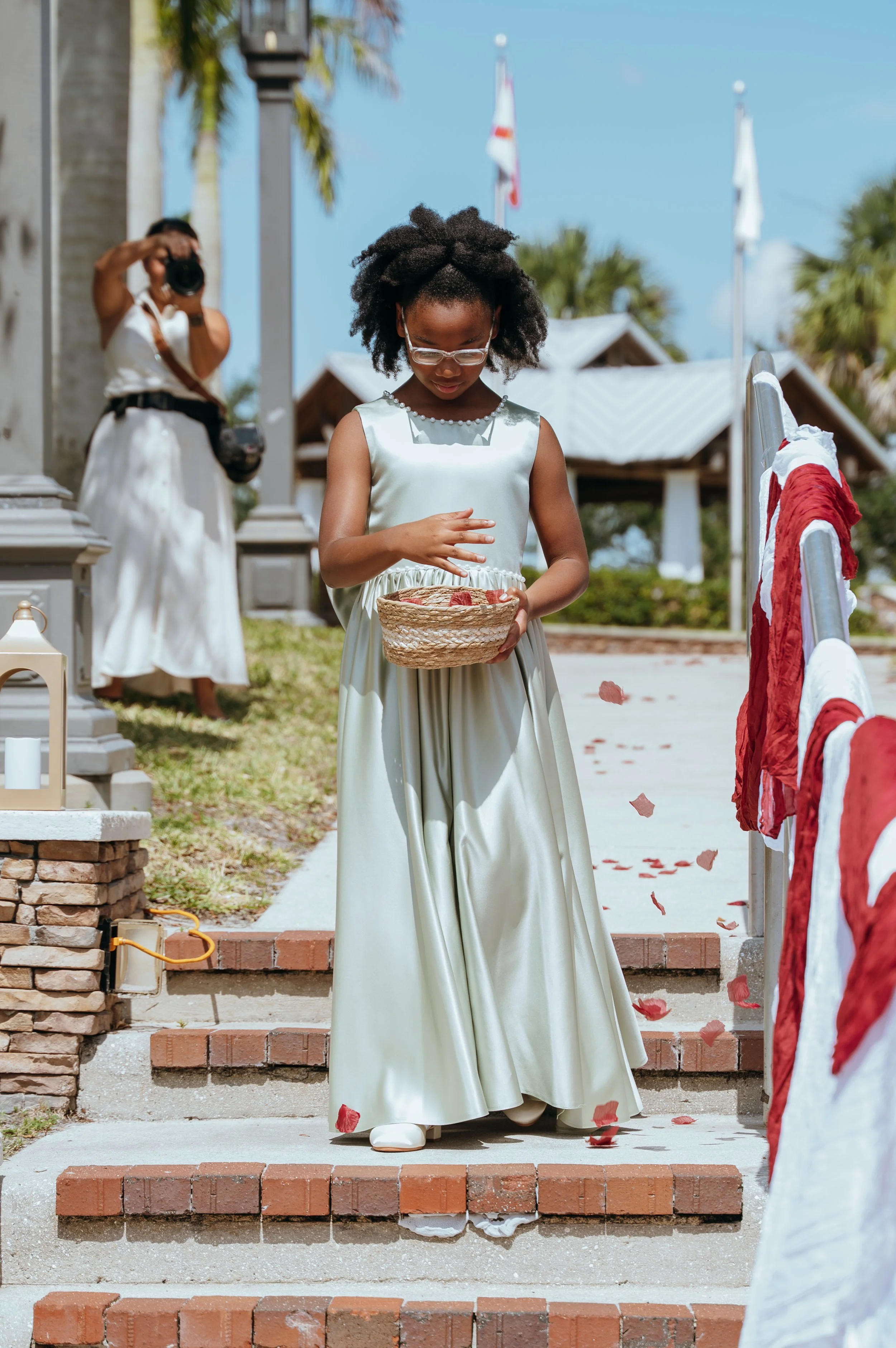 Flower girl in a sage green dress scattering burgundy rose petals at the Waters wedding ceremony.