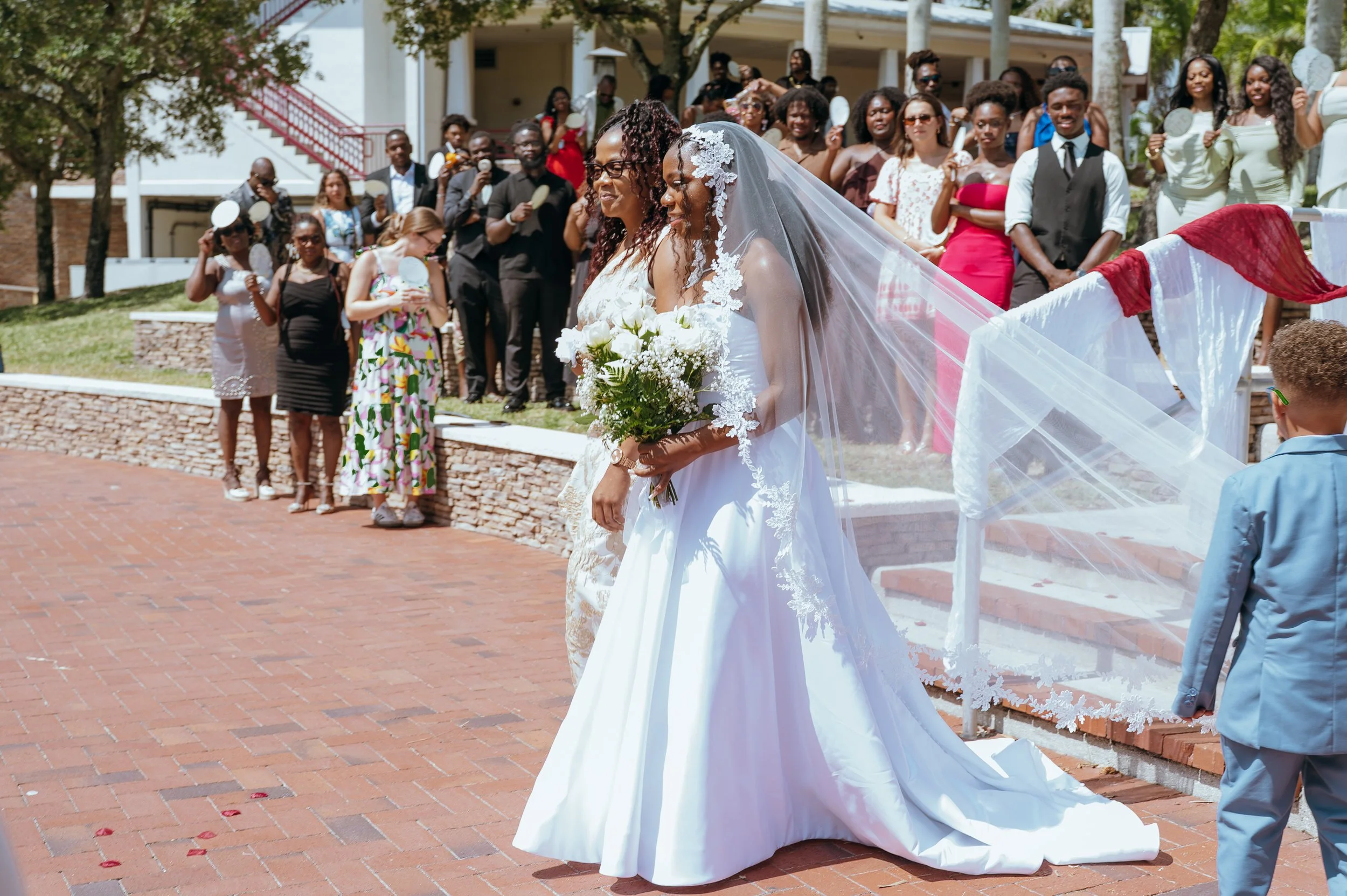 Bride Anndi Waters walking toward her outdoor wedding ceremony with her long veil flowing behind her.