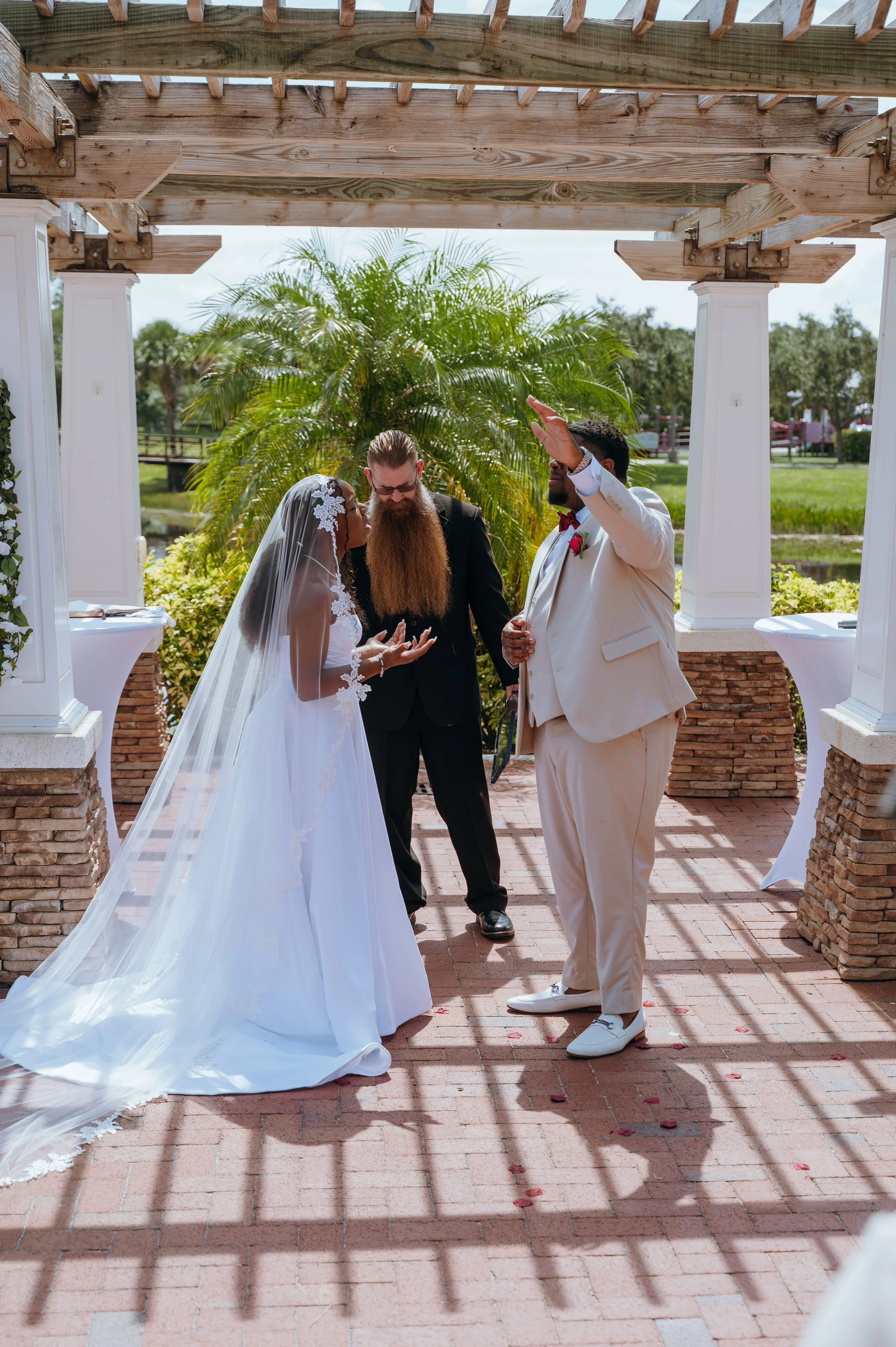 Diego raising his hand in worship beside Anndi and their officiant during their outdoor wedding ceremony.