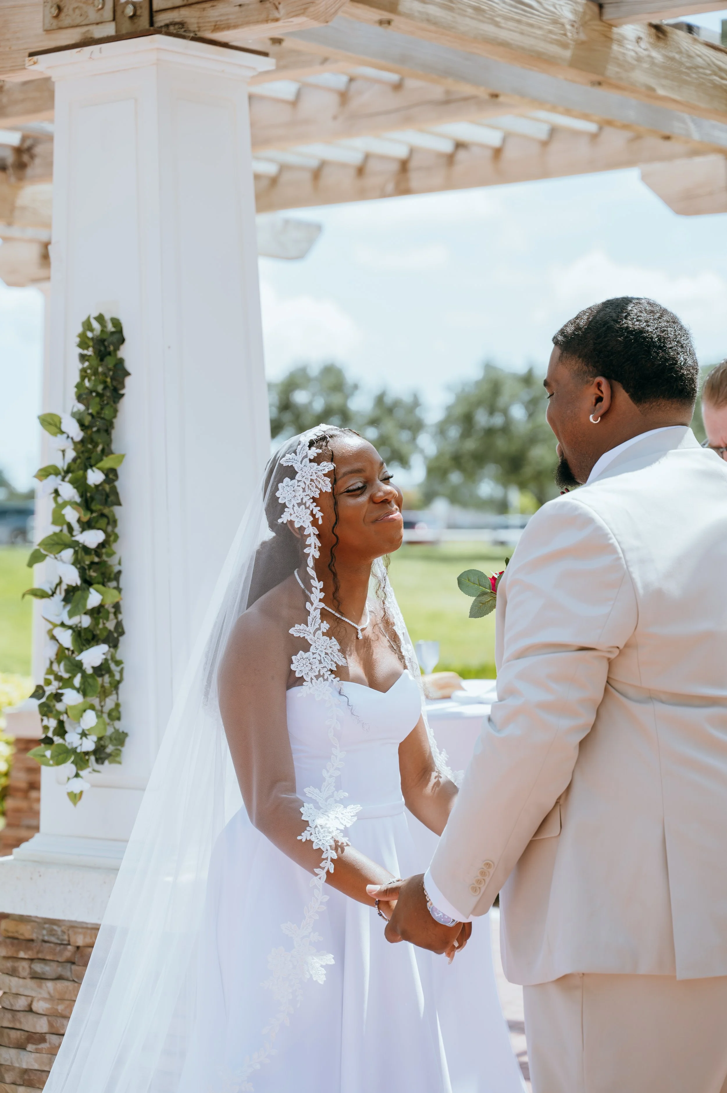 Anndi smiling at Diego while they hold hands beneath the wedding pergola.
