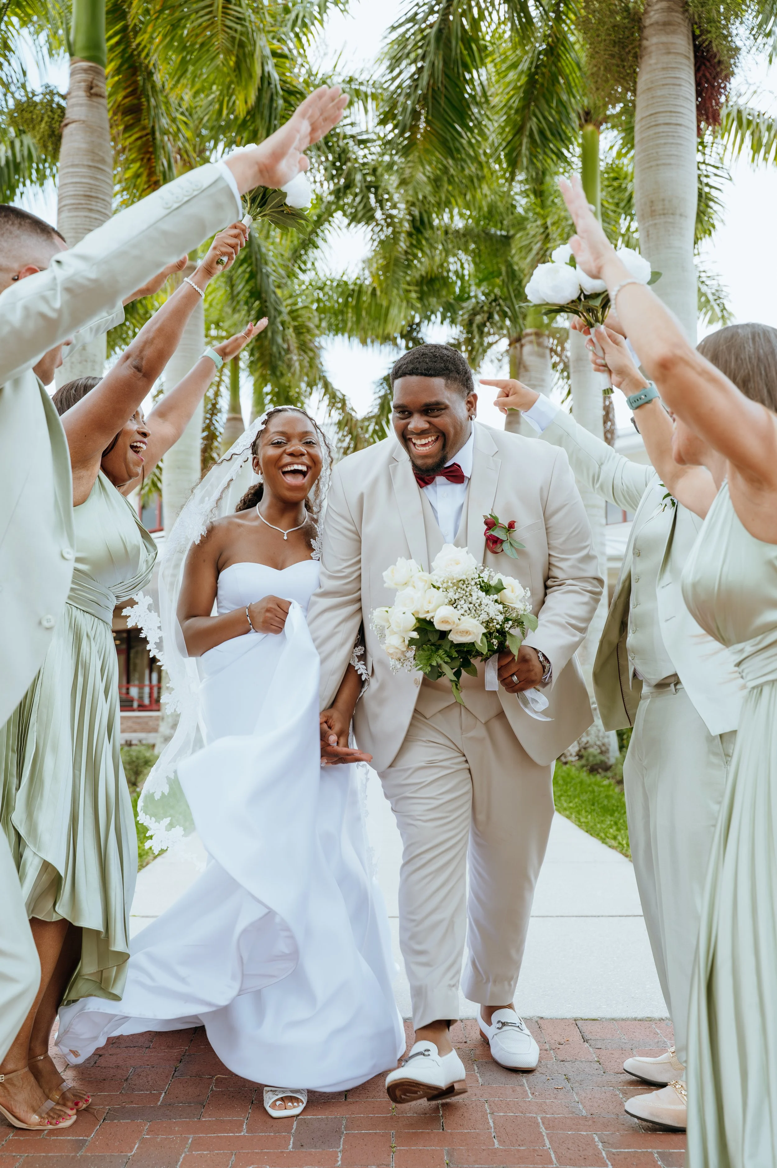 Anndi and Diego Waters laughing as their wedding party cheers them on beneath palm trees at Royal Palm Beach Commons Park.