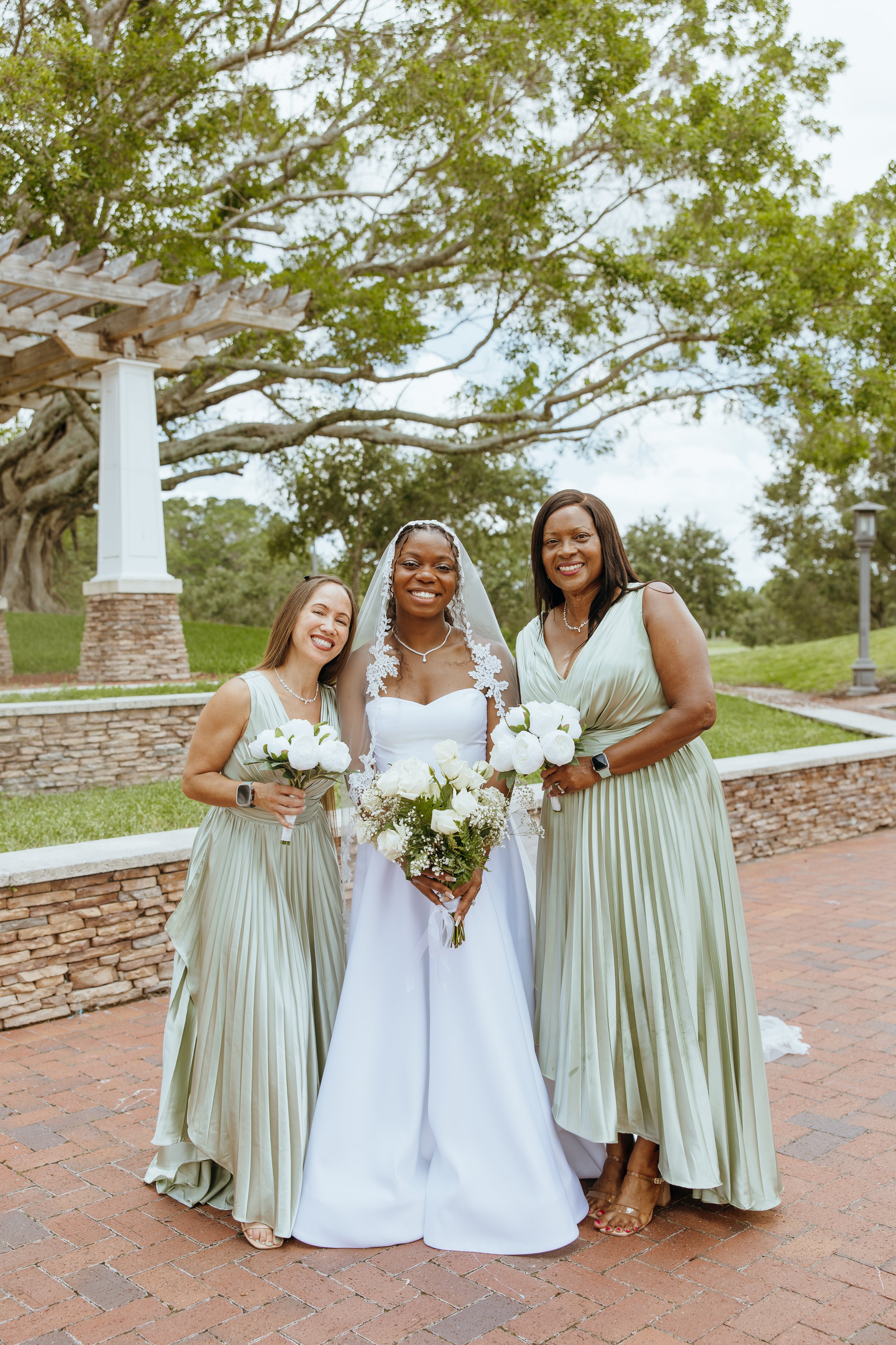 Anndi Waters standing between two bridesmaids wearing sage green dresses and holding white floral bouquets.