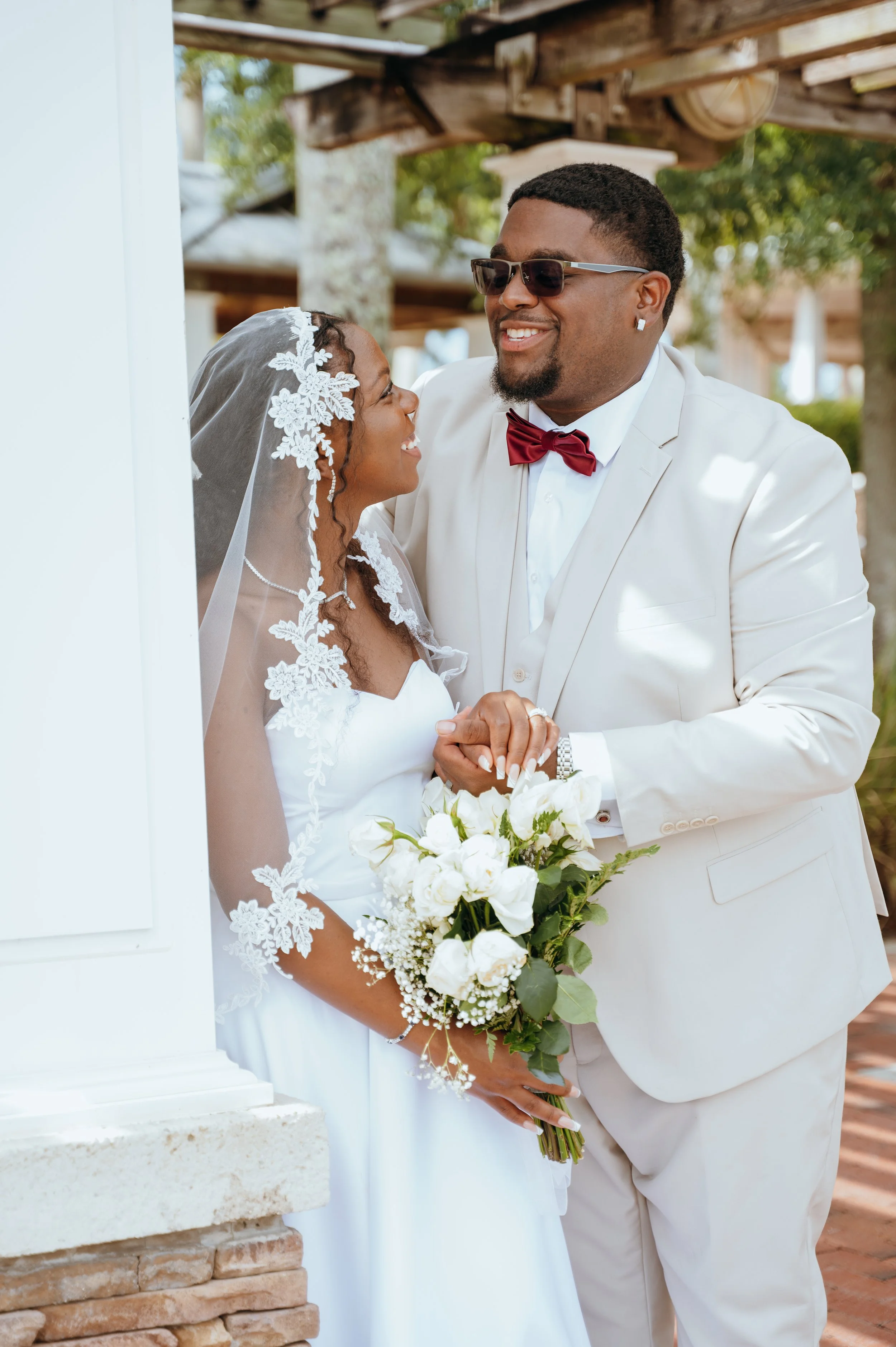 Anndi and Diego laughing together beside a white column during their wedding portraits.