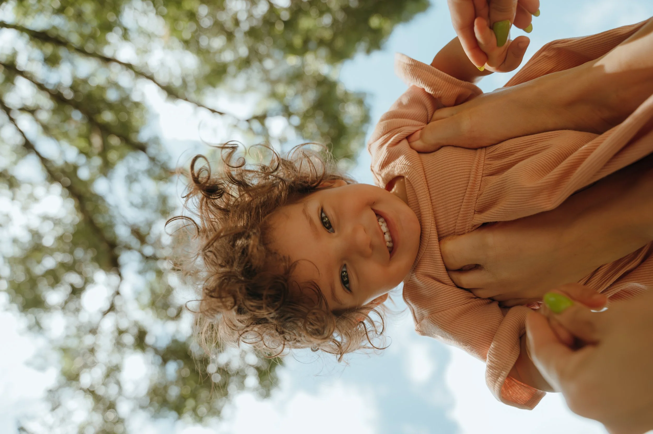 Curly-haired child smiling down toward the camera during a playful outdoor Palm Beach family session.