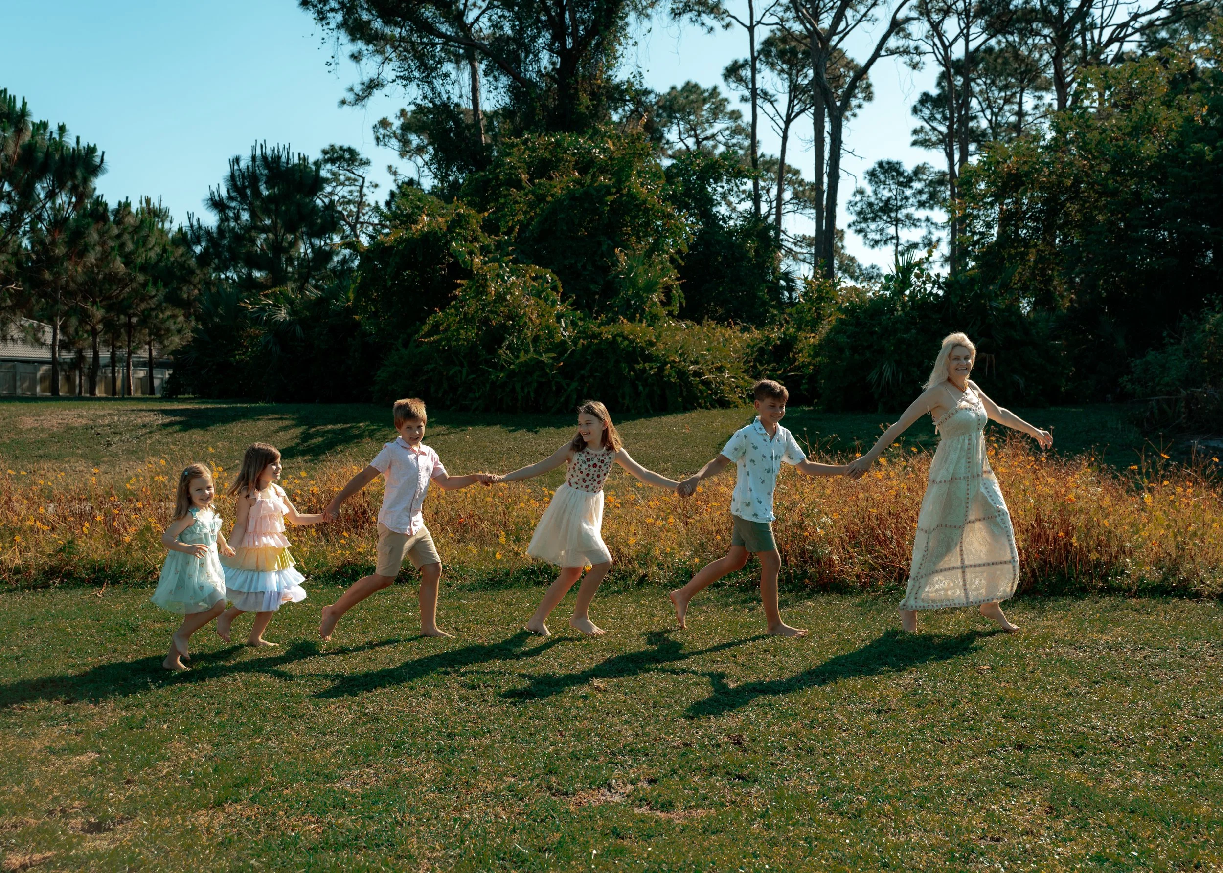 Mother holding hands with her children as they walk through a sunlit field at Barwick Park in Delray Beach, Florida.