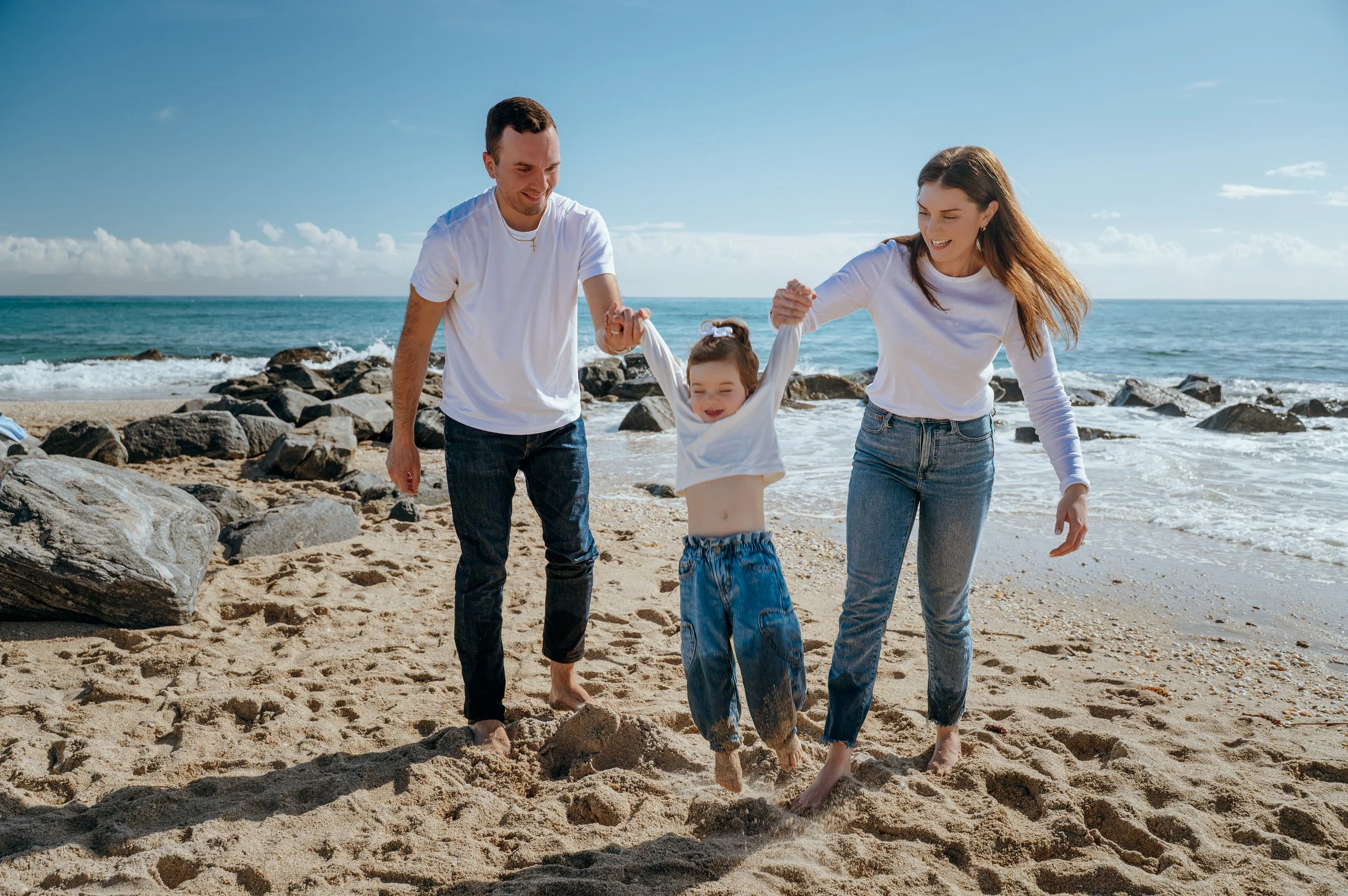 Parents lifting their daughter by the hands during a playful Palm Beach family beach photography session
