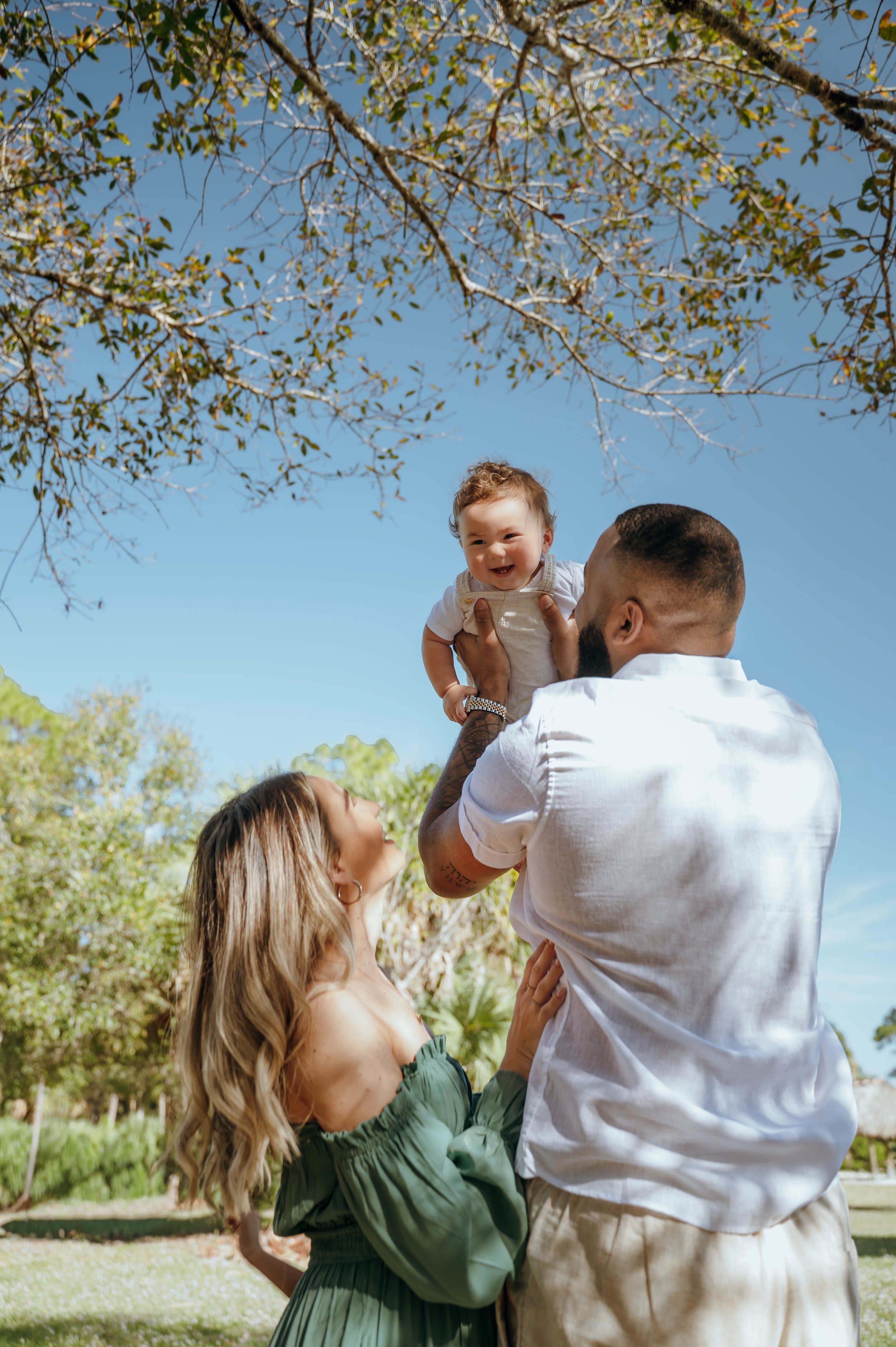 Parents smiling up at their baby during a playful outdoor family photography session in Palm Beach County, Florida.