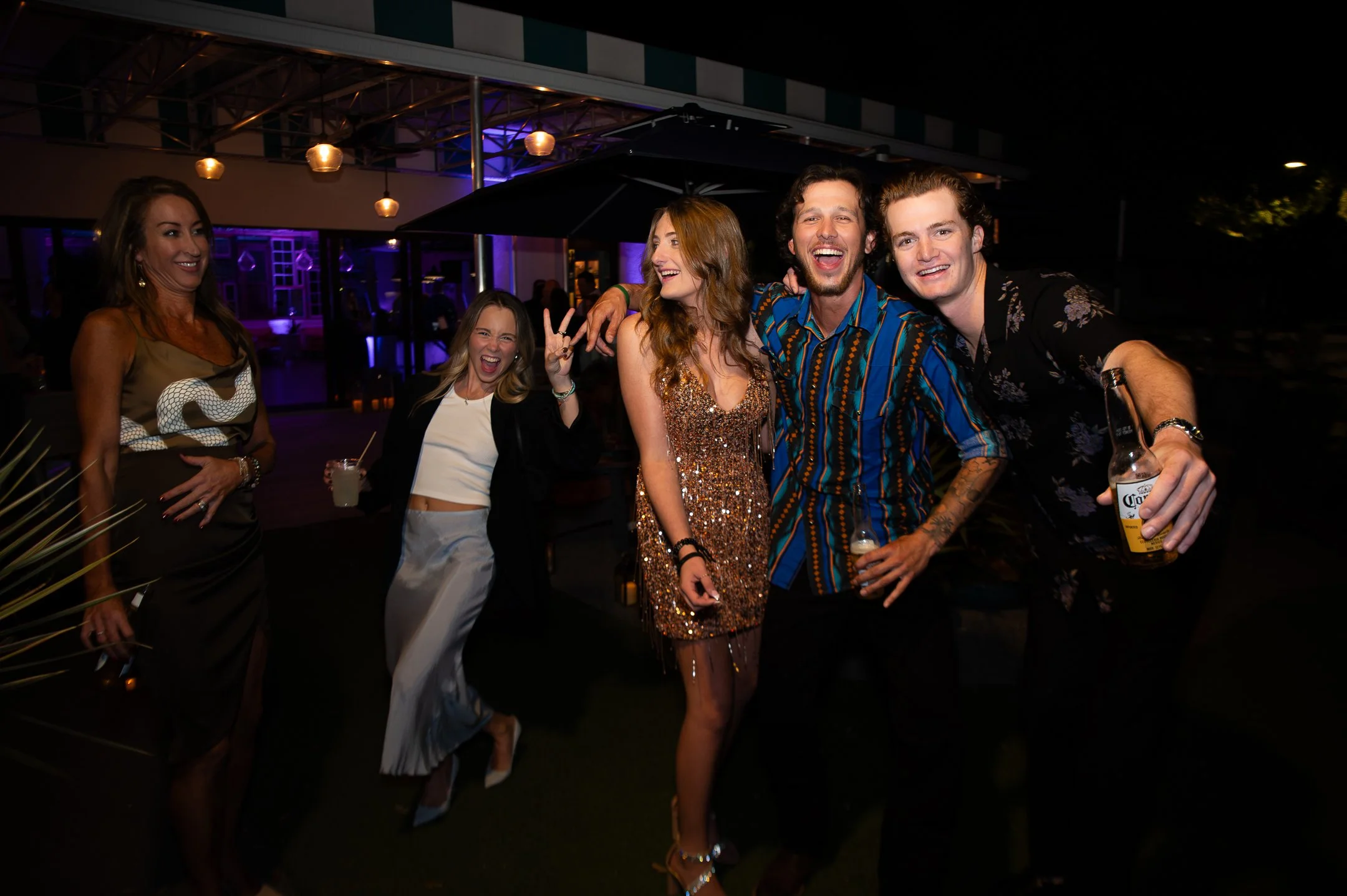 Group of five friends smiling and having fun at night during a party, with some holding drinks.
