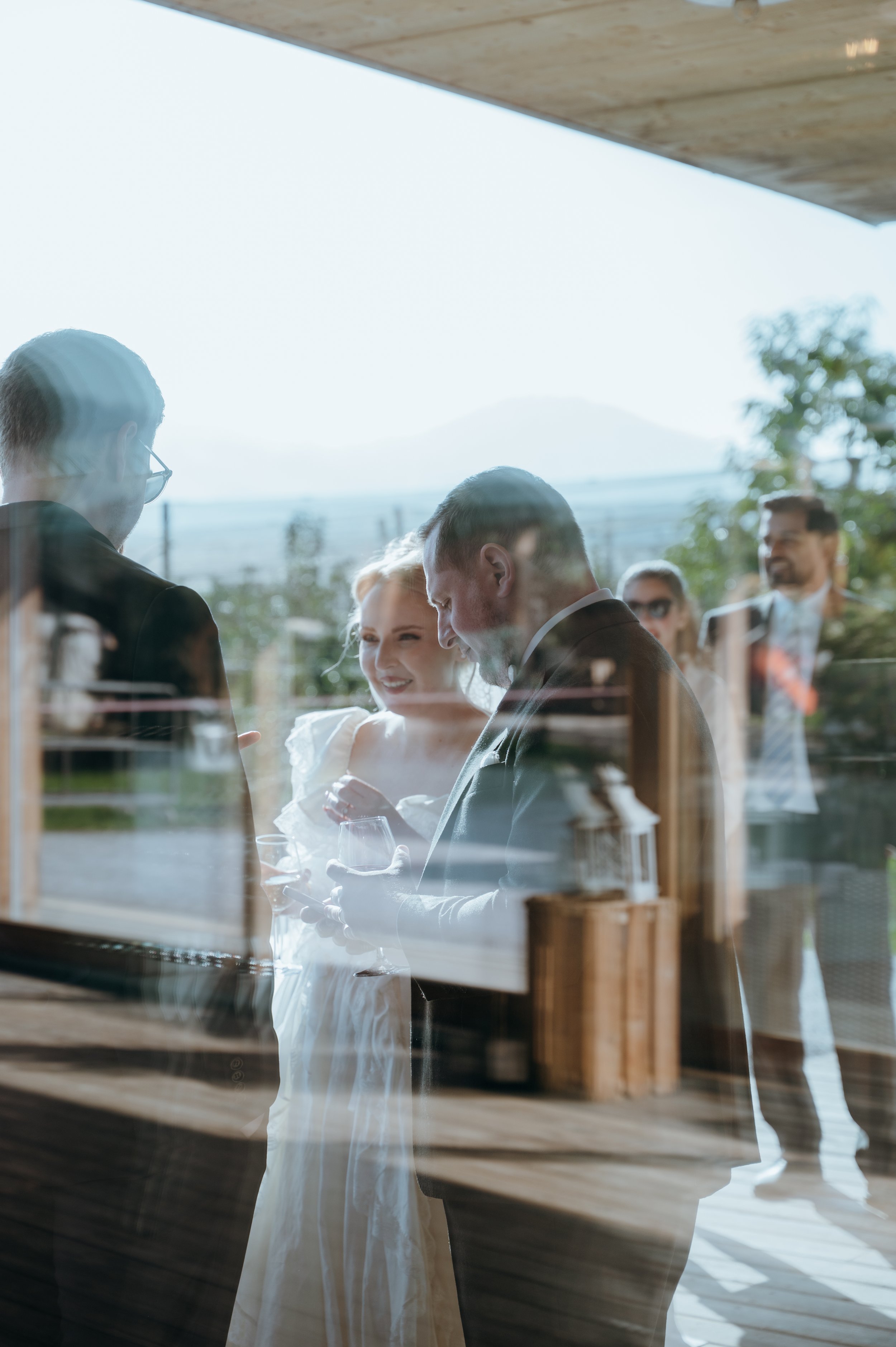 Malwina and Matthew reflected in the venue windows while spending cocktail hour with their wedding guests in Switzerland