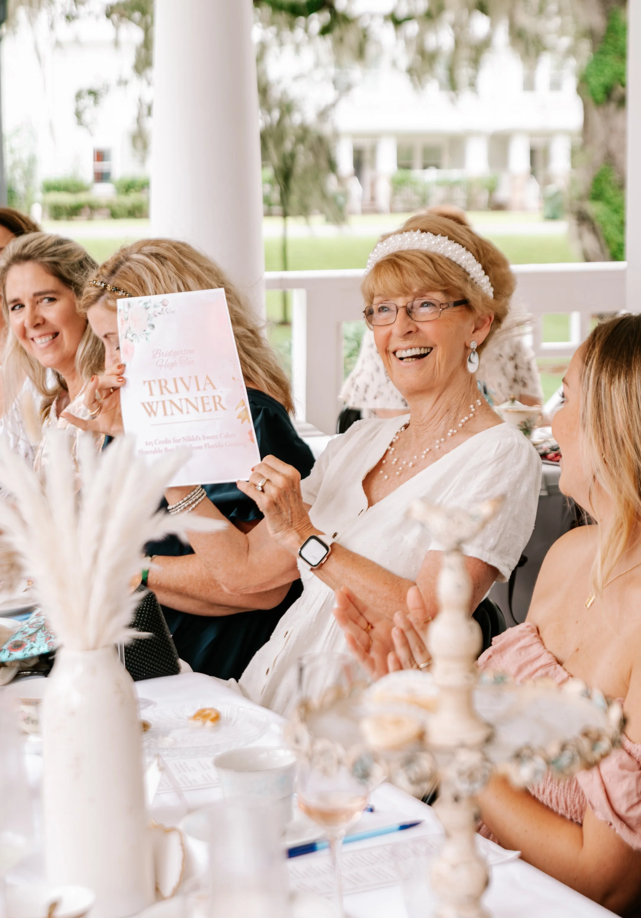 Smiling guest holding her trivia winner sign during a Bridgerton-inspired high tea event.
