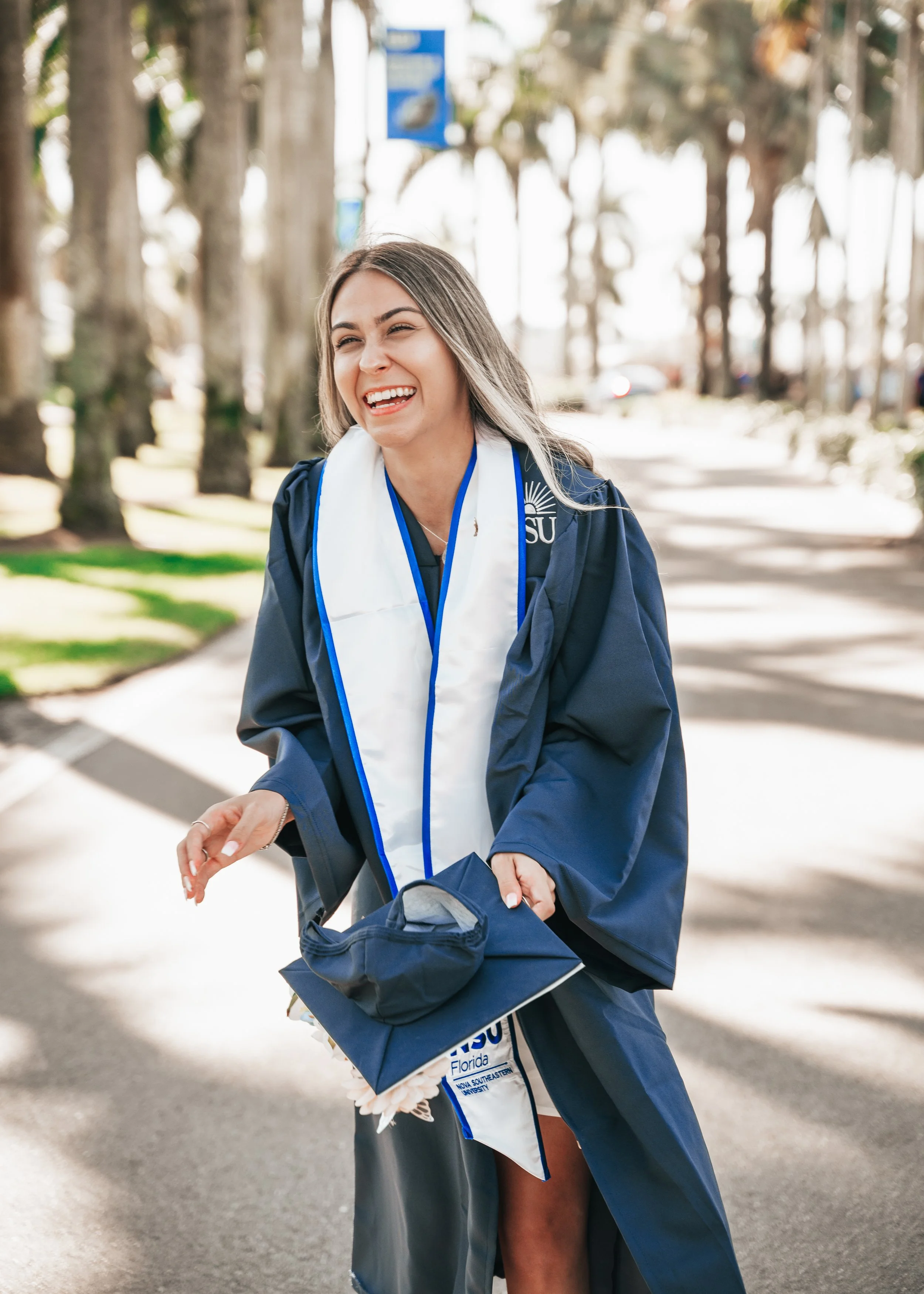Nova Southeastern University graduate laughing in her cap and gown during a graduation portrait session on campus in Davie, Florida.