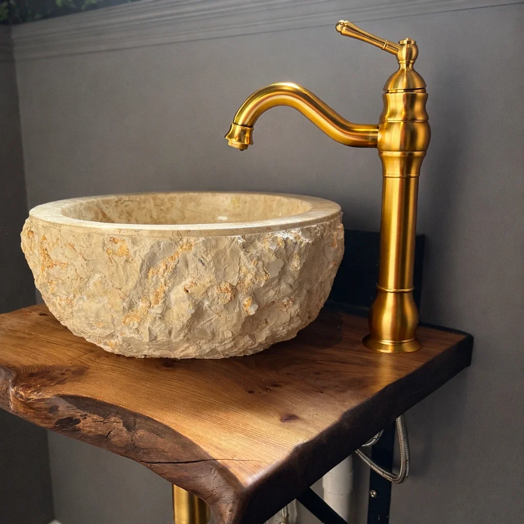 A rustic bathroom sink with a natural stone bowl and a gold basin on a wooden countertop.