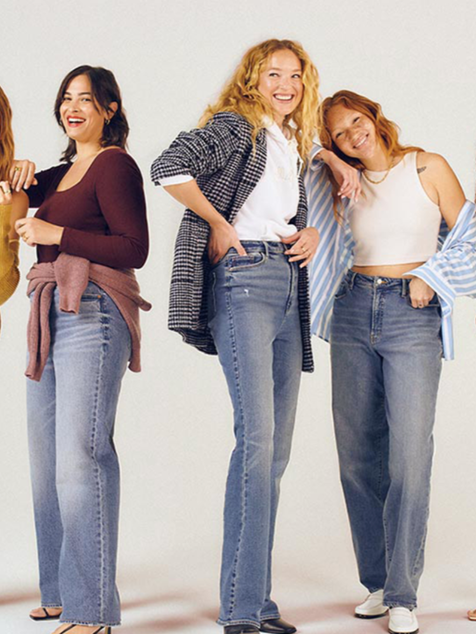 Group of diverse smiling women standing together against a plain background, dressed casually.