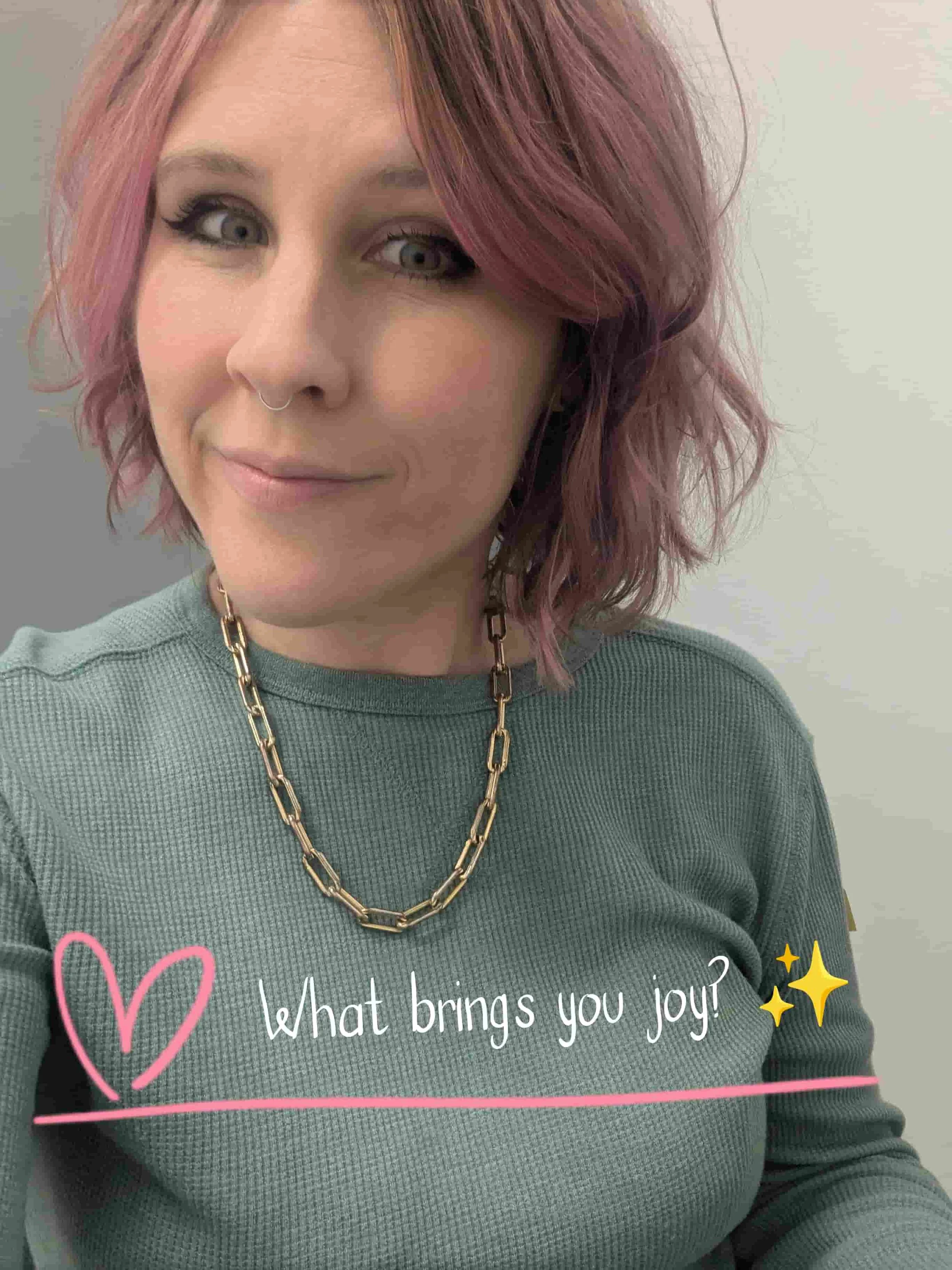 Anxiety Therapist Christin Trott. A woman with pinkish hair and a septum ring wearing a pale green shirt and gold chunky chain necklace, smiling at the camera.
