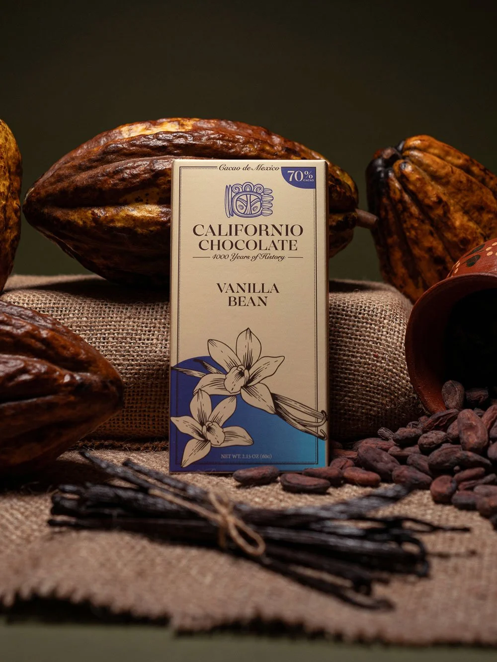 Bar of Californio Chocolate Vanilla Bean 70% dark chocolate surrounded by cacao beans, pods, and vanilla beans on burlap