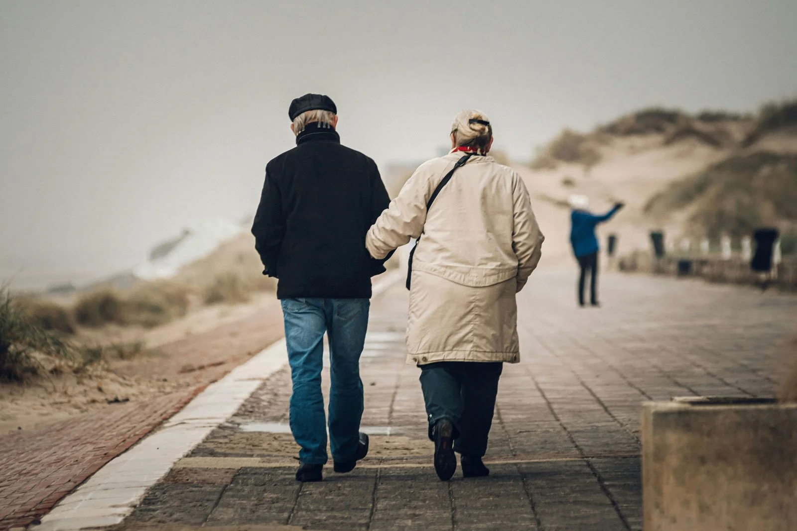 An older couple walks side by side along a quiet boardwalk, moving forward together while navigating estrangement from an adult child.