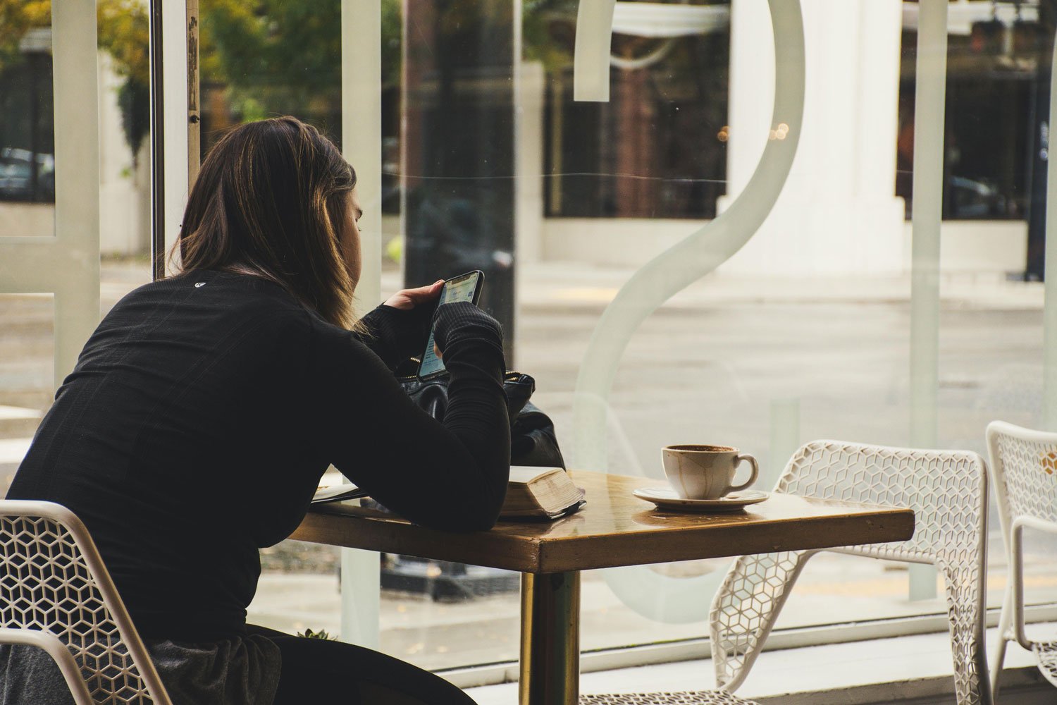 A woman sits alone at a coffee shop, an empty chair beside her, reflecting the quiet grief of friendship loss.