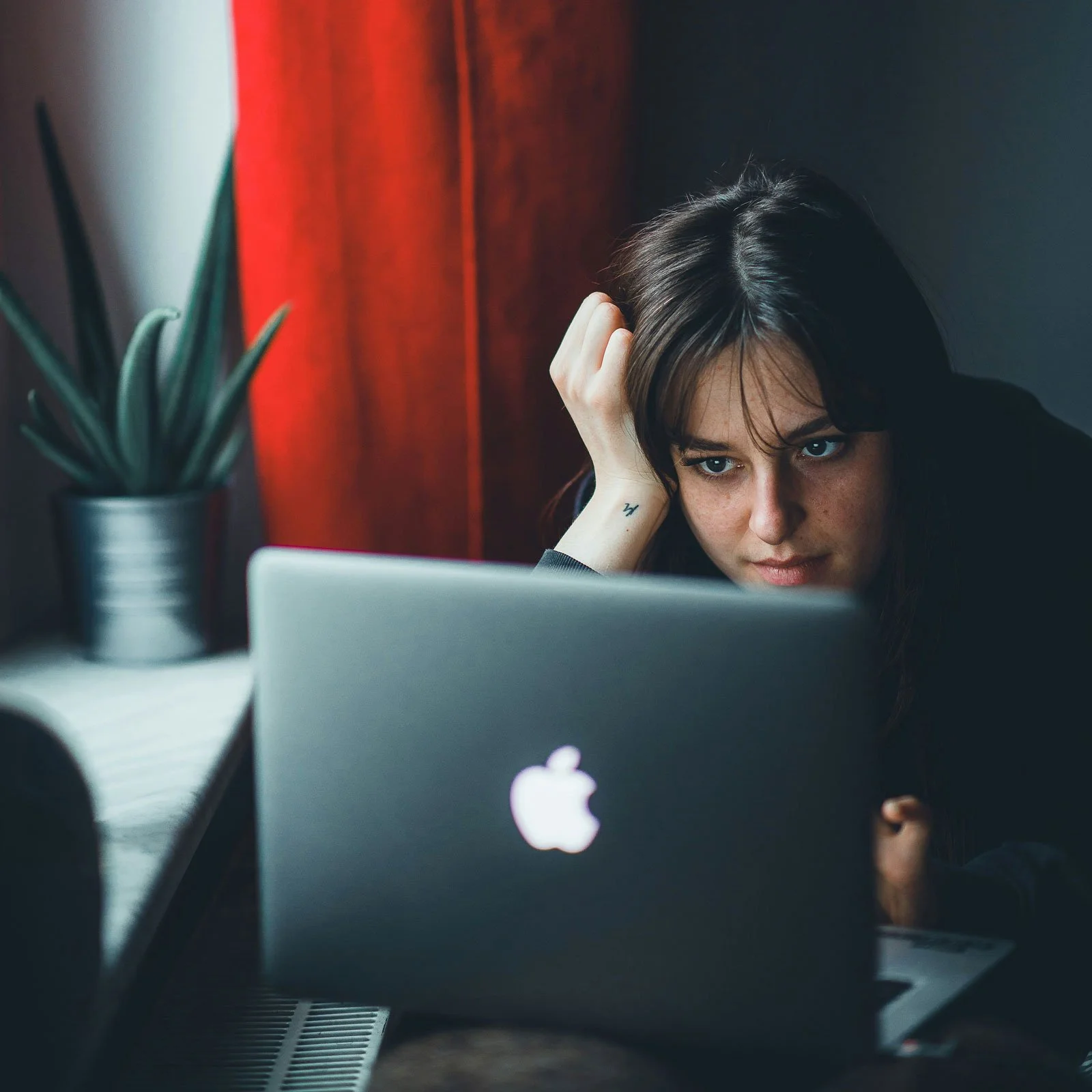 Woman sitting at a laptop with her hand resting against her head, looking at the screen with a thoughtful expression — representing the experience of reaching out for grief counseling online