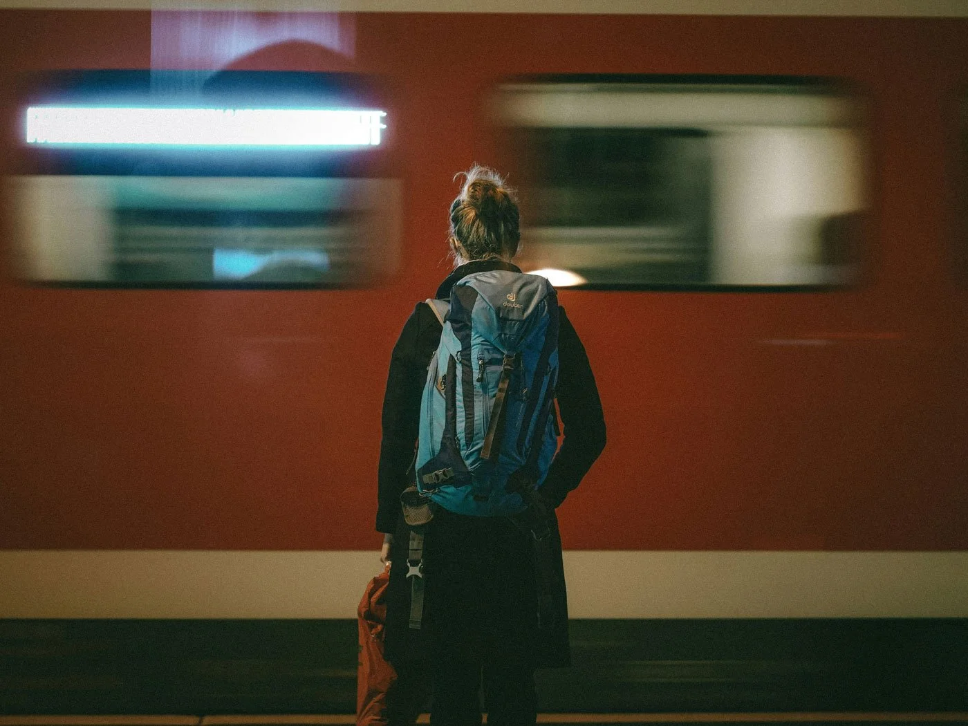 Woman standing alone on a train platform with her back to the camera, a train passing in a blur beside her — conveying the quiet isolation of estrangement grief