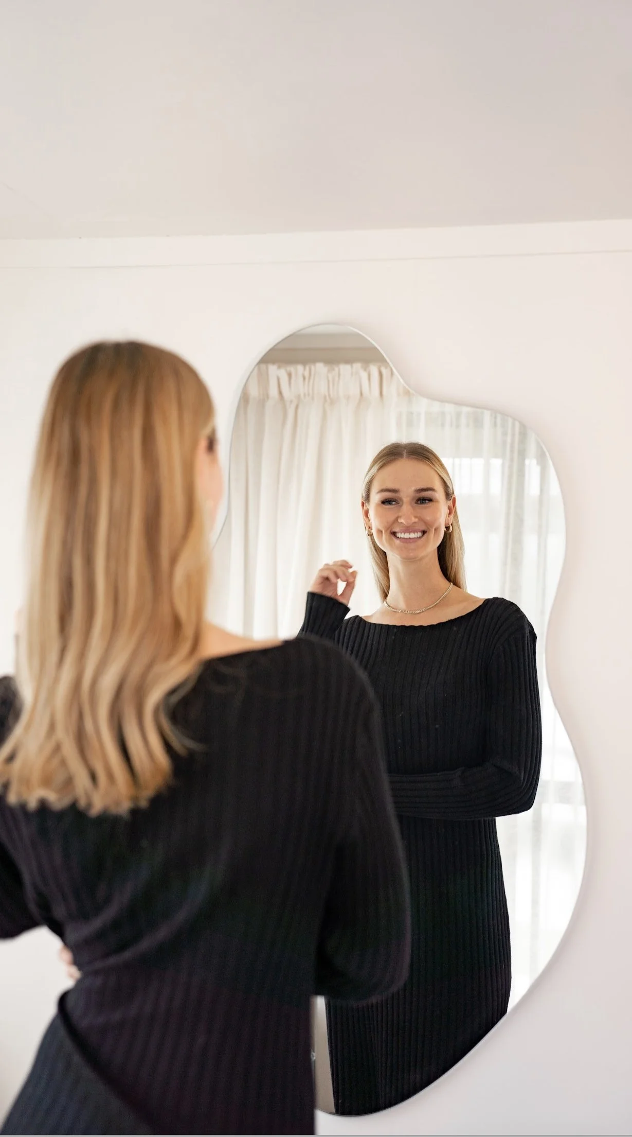 Woman with blonde hair looking at herself in a mirror and smiling before laser tattoo removal service.