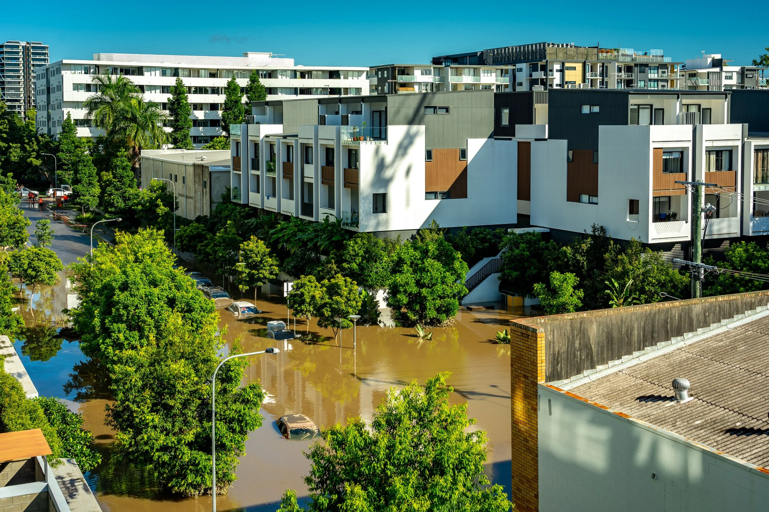 Cars submerged under floodwaters on street with apartment buildings.
