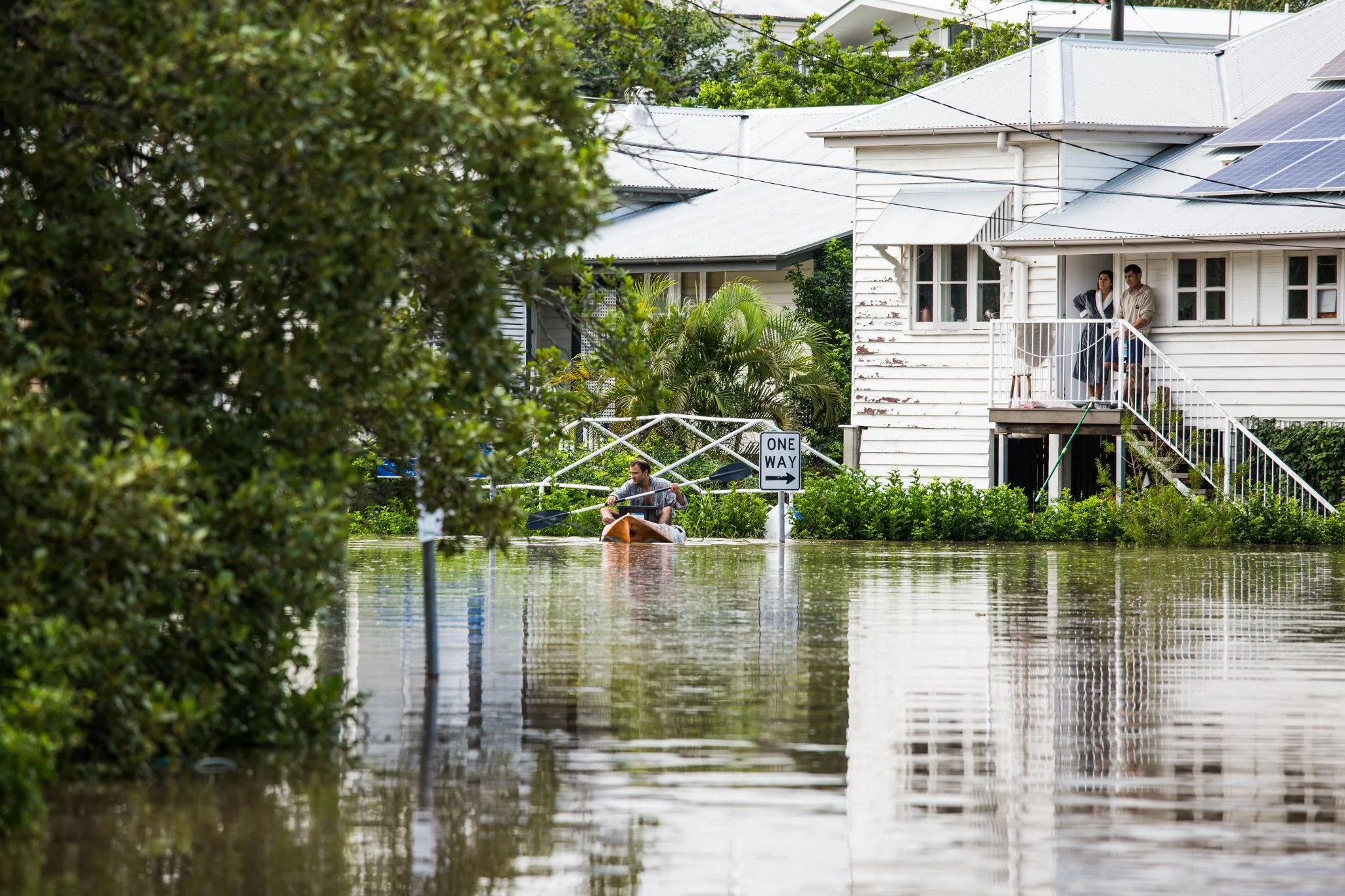 Two people stand on their front doorstep of their house surrounding by floodwaters.