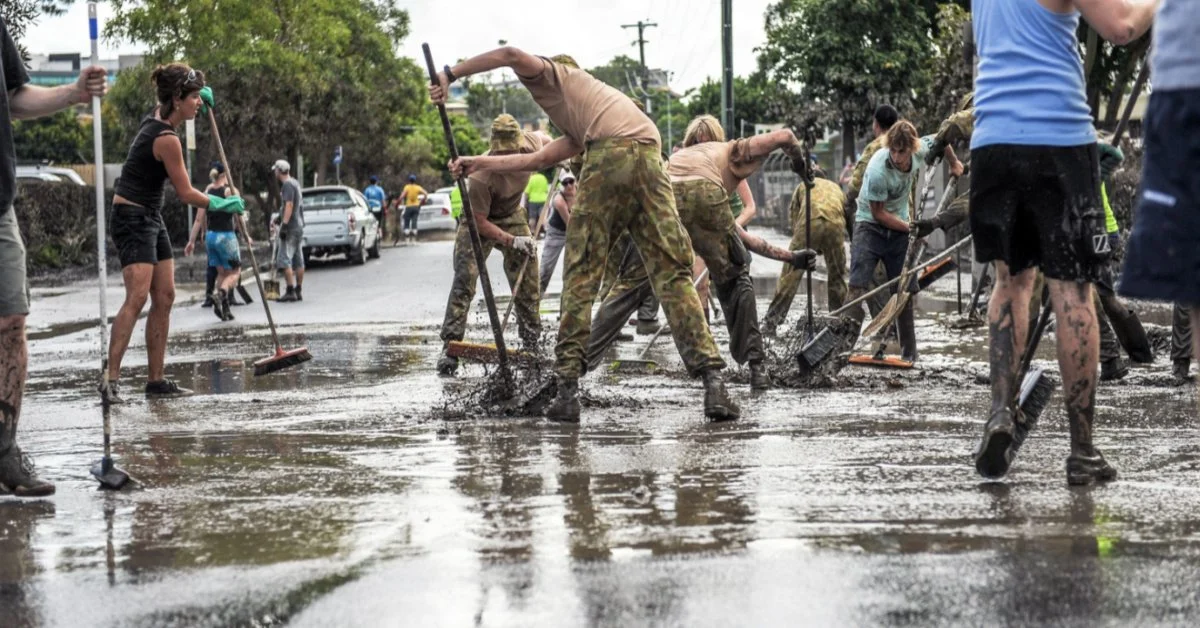 Volunteers sweep mud on street.