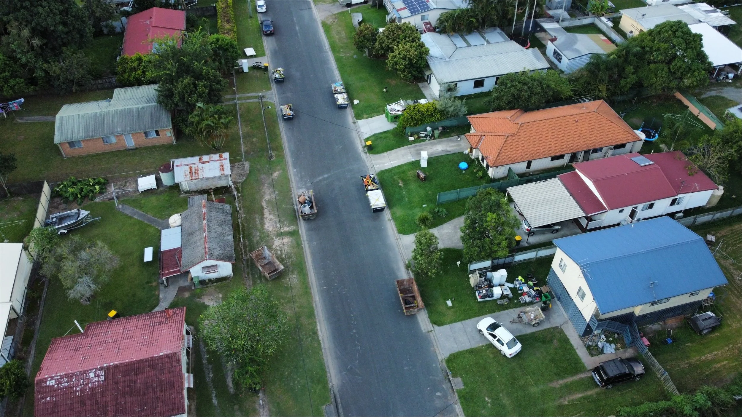 An aerial shot of a street of houses with rubbish piles outs the front from flood damage.
