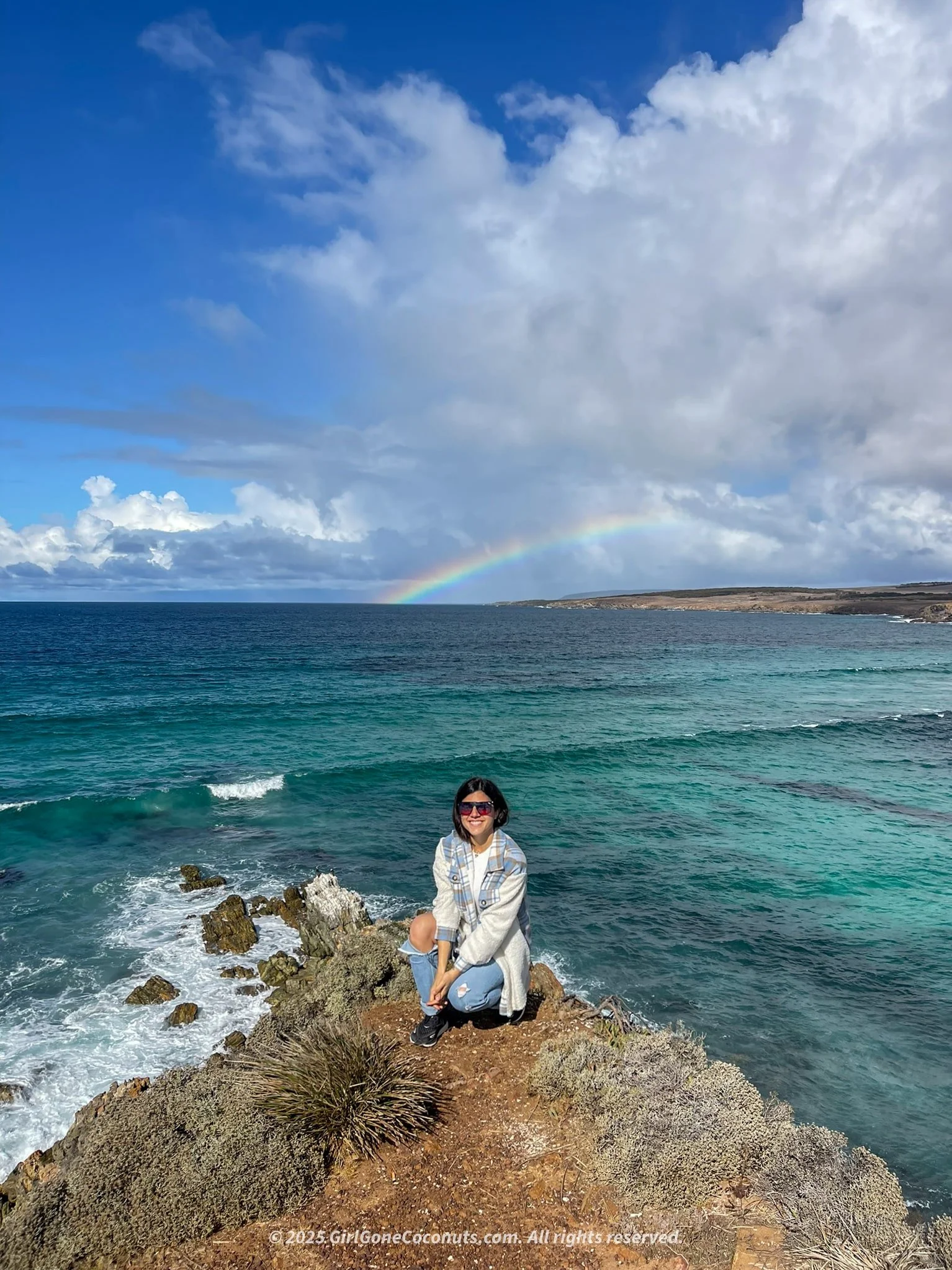 Traveler standing atop a viewpoint overlooking Port Lincoln's coastline with a rainbow in the backdrop.