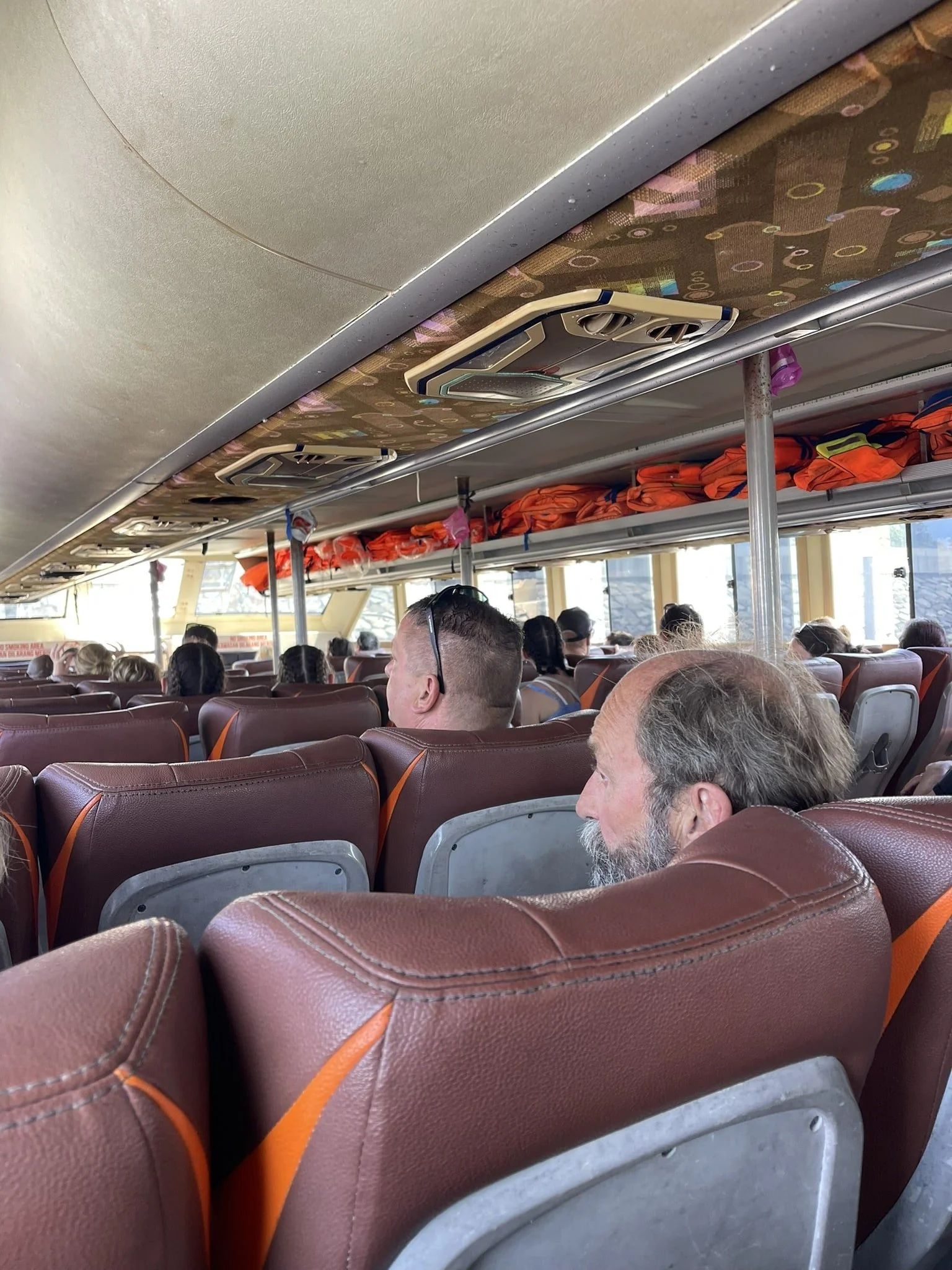 Packed interior of a Bali to Lombok speedboat with passengers and life jackets overhead.