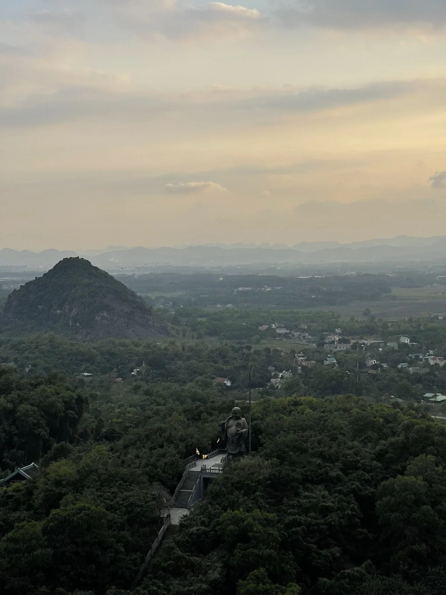 Panoramic sunset view over Ninh Binh from Bao Thap Tower at Bai Dinh Pagoda, with Maitreya Buddha statue in the foreground.