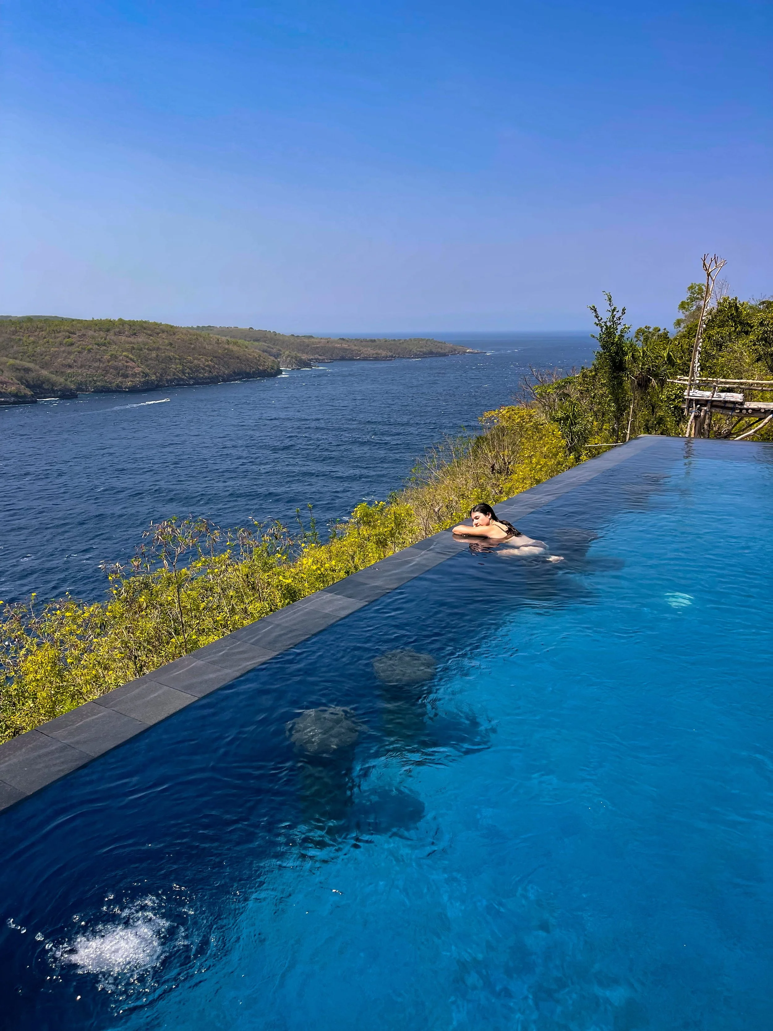 Traveler sunbathing and cooling off in the infinity pools at Ceningan Cliffs.